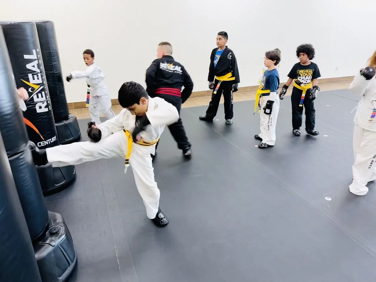 Kids in martial arts class practicing kicks on kicking bags at Reveal Martial Arts.