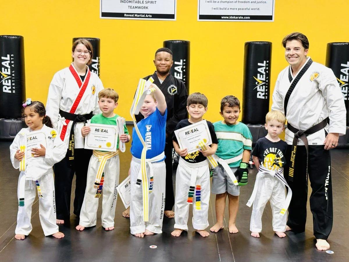 Reveal Martial Arts instructors standing with a group of students with big smiles and happy faces.