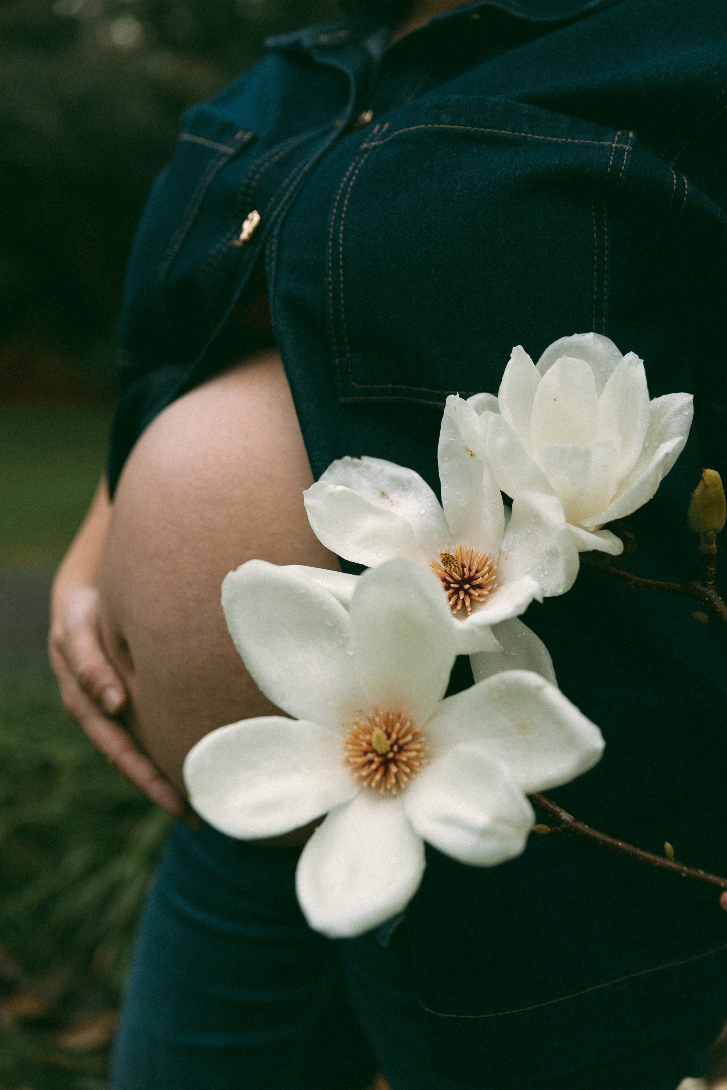 Person wearing dark denim shorts, holding white magnolia flowers.