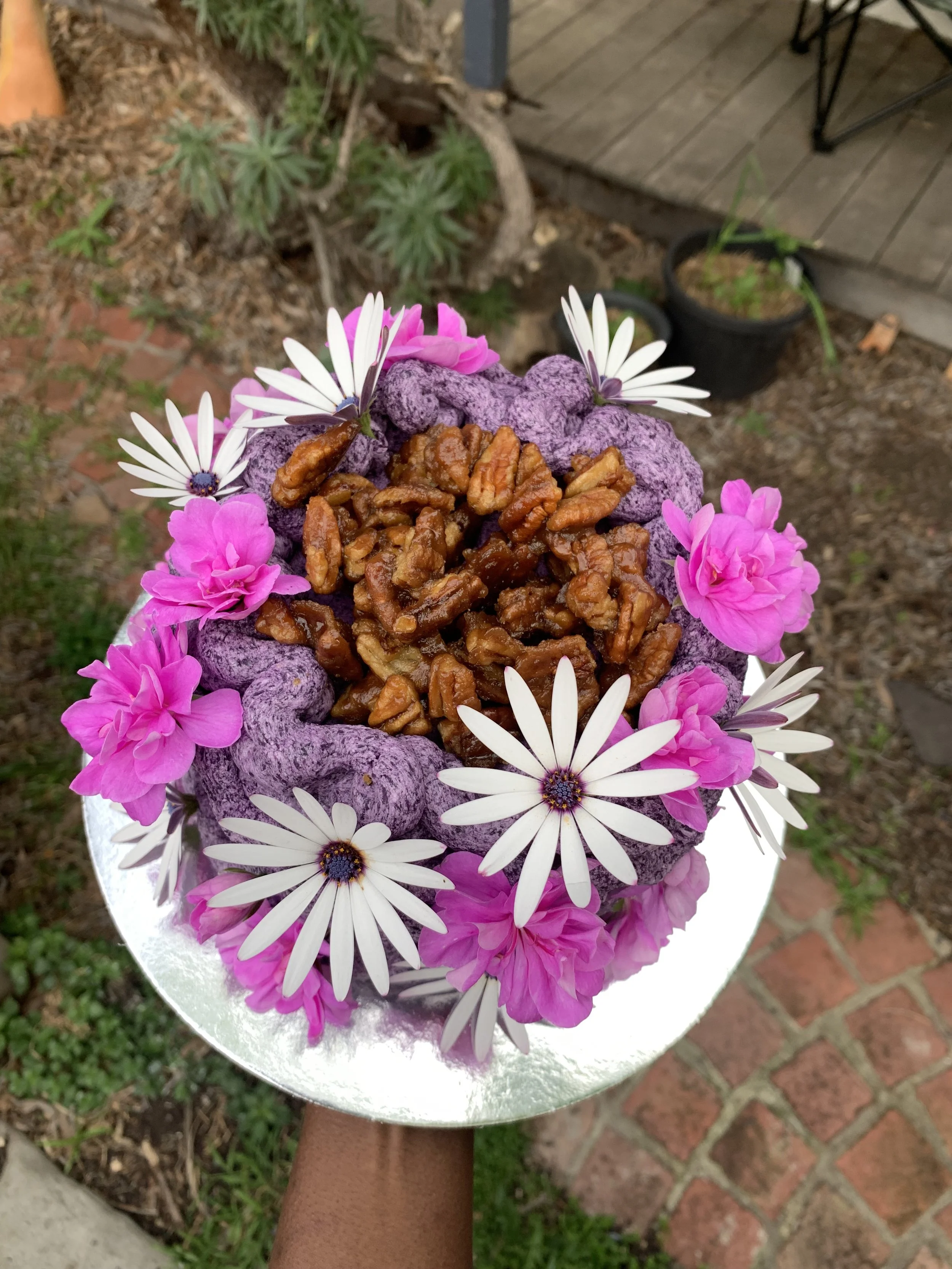 A cake decorated with purple and pink flowers and topped with walnut pieces.