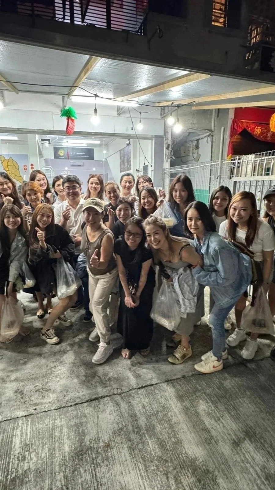 Group of smiling women and men gathered outside at night, posing for a photo.