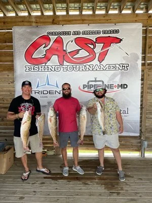 Three men holding large fish in front of a sign for a fishing tournament.