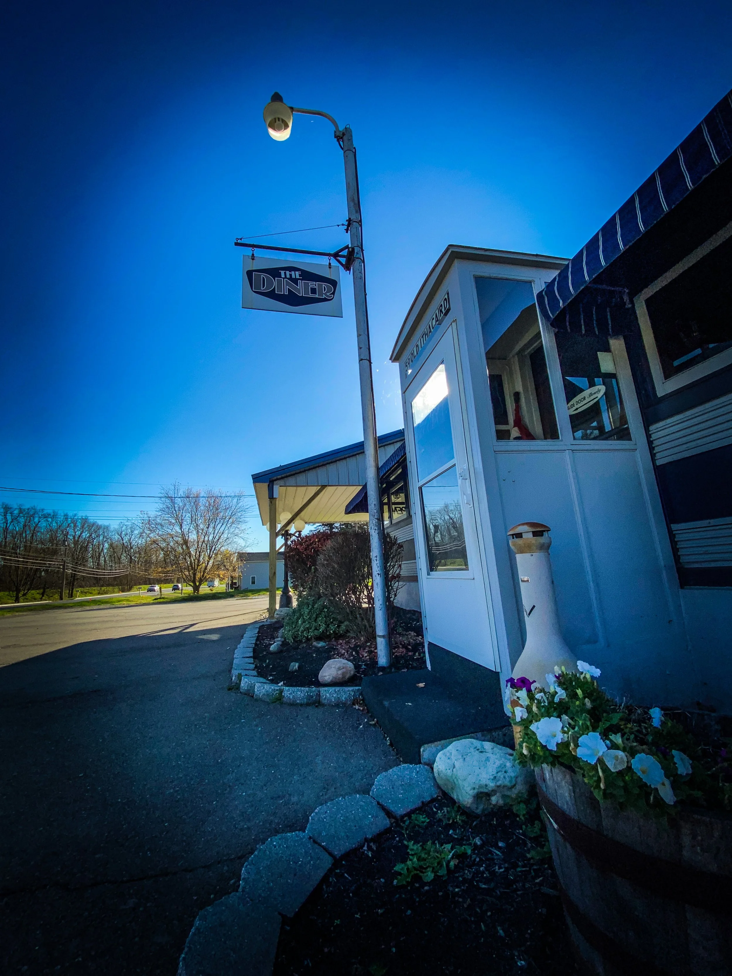 Exterior of a diner with a hanging sign, outdoor light post, and flower pot in front.