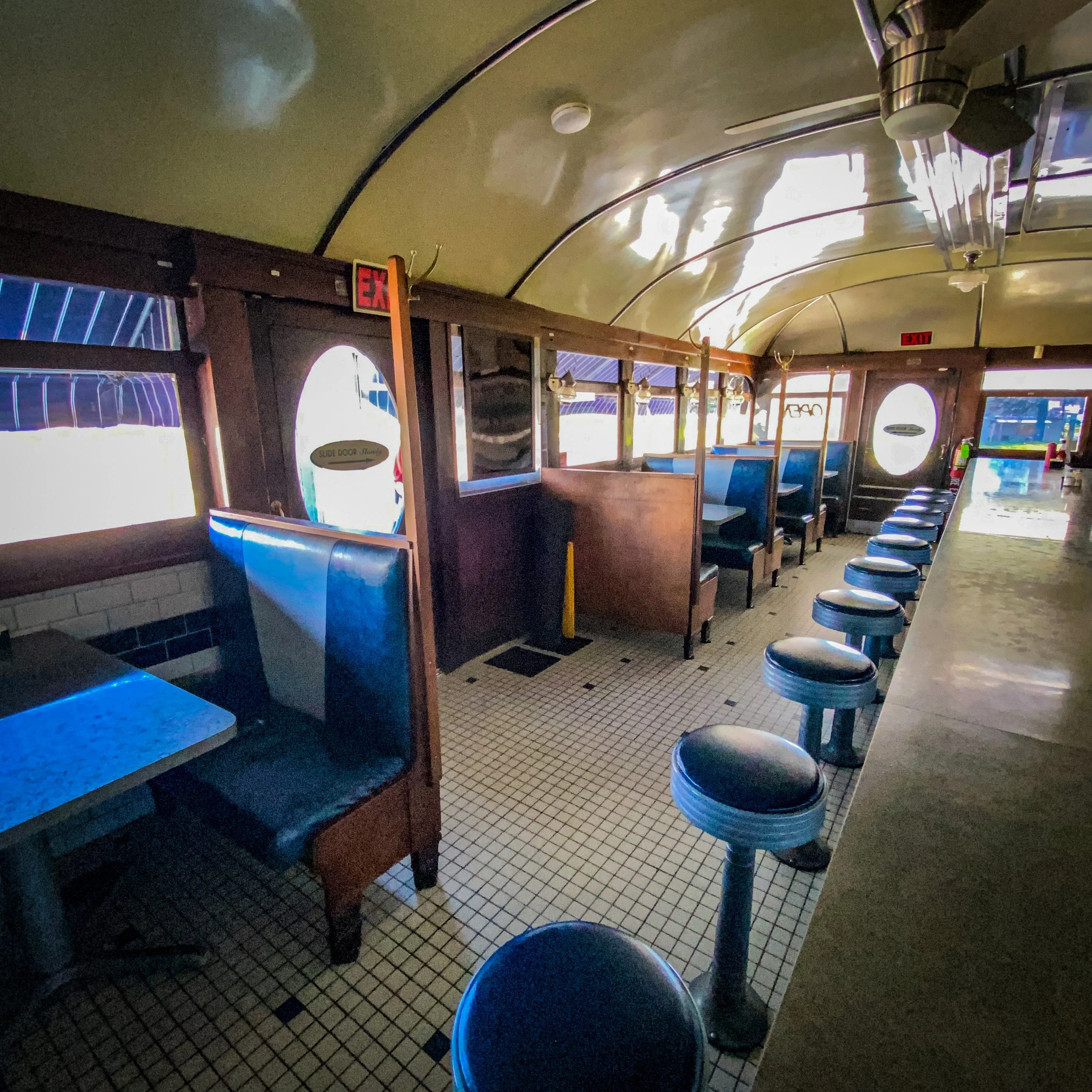Interior of a vintage diner with blue booths, counter stools, and a tiled floor.