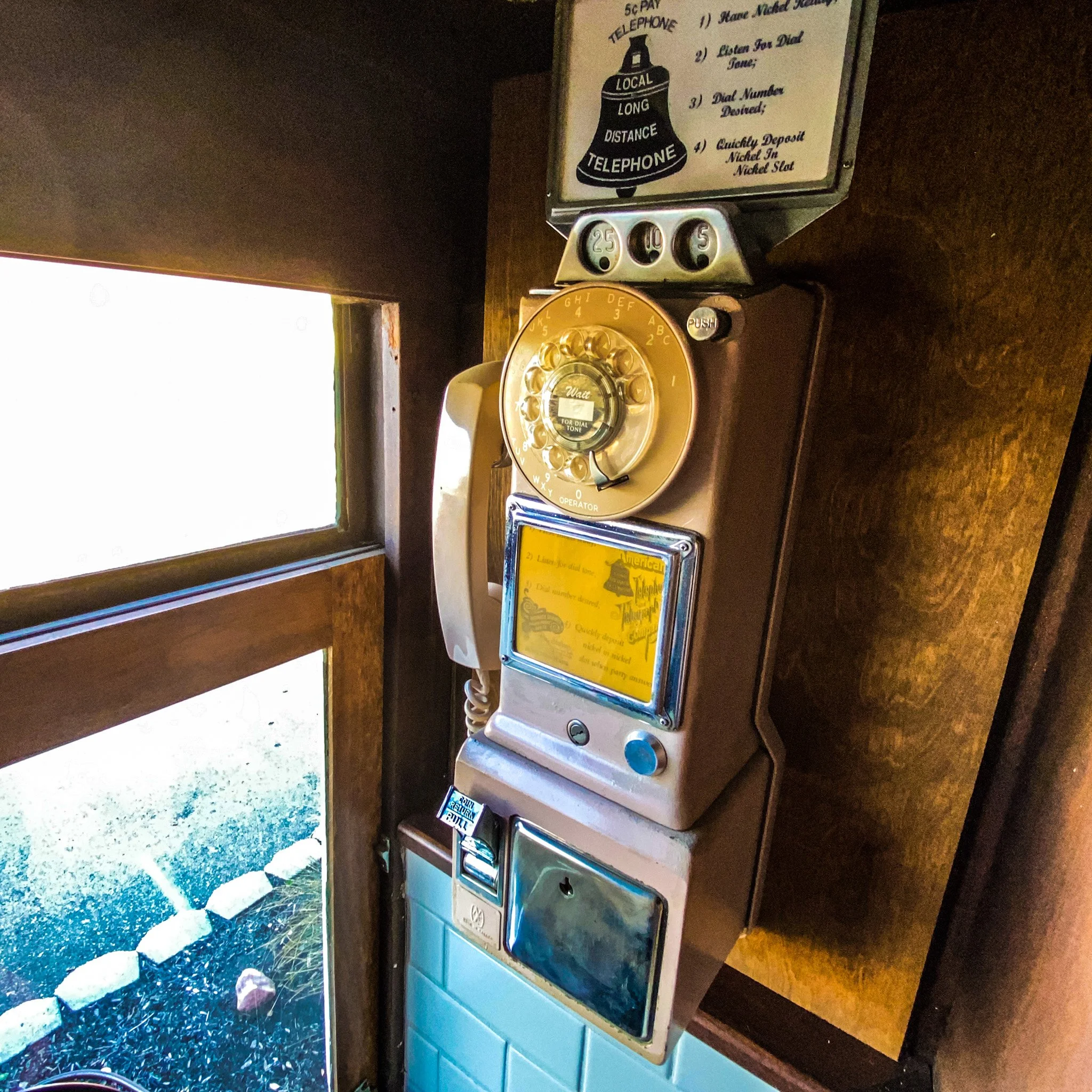 Vintage rotary payphone on a wall in a wooden booth, featuring a coin slot and instructions for use.