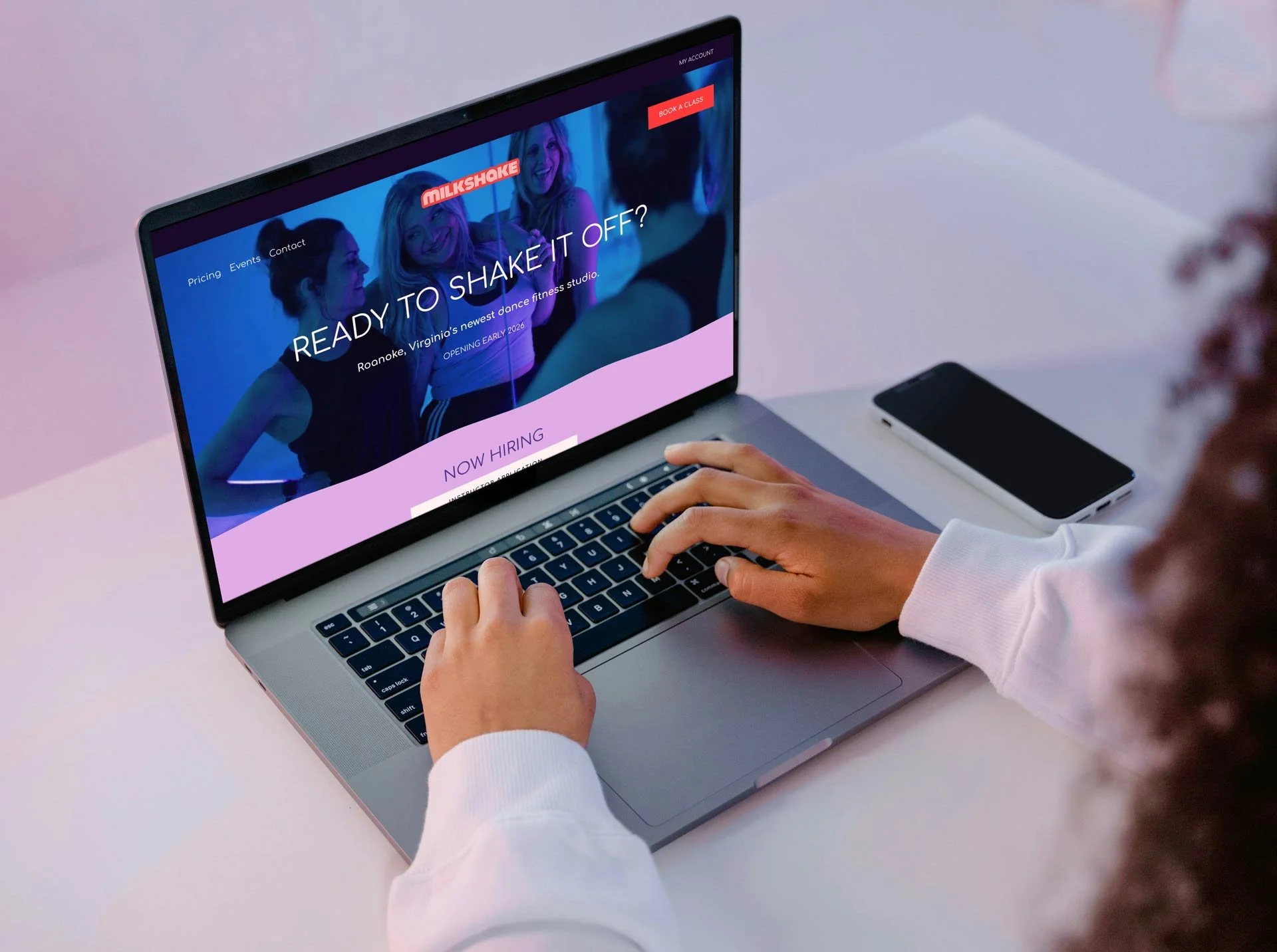 Person browsing a fitness studio website on a laptop, with a smartphone on the desk, promoting dance fitness classes in Roanoke, Virginia.