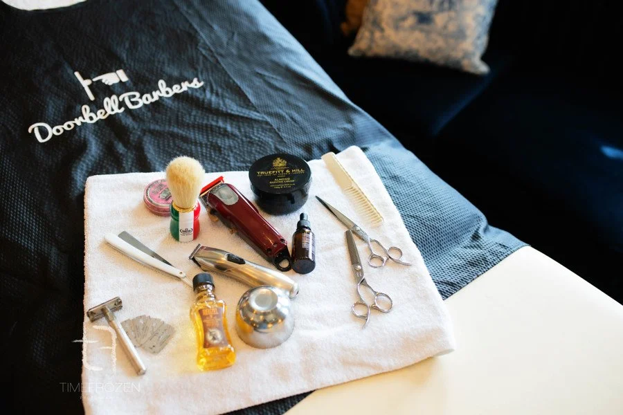 Barber tools and grooming supplies on a towel, including scissors, razors, comb, shaving cream, and a brush, with "Doorbell Barbers" branding.