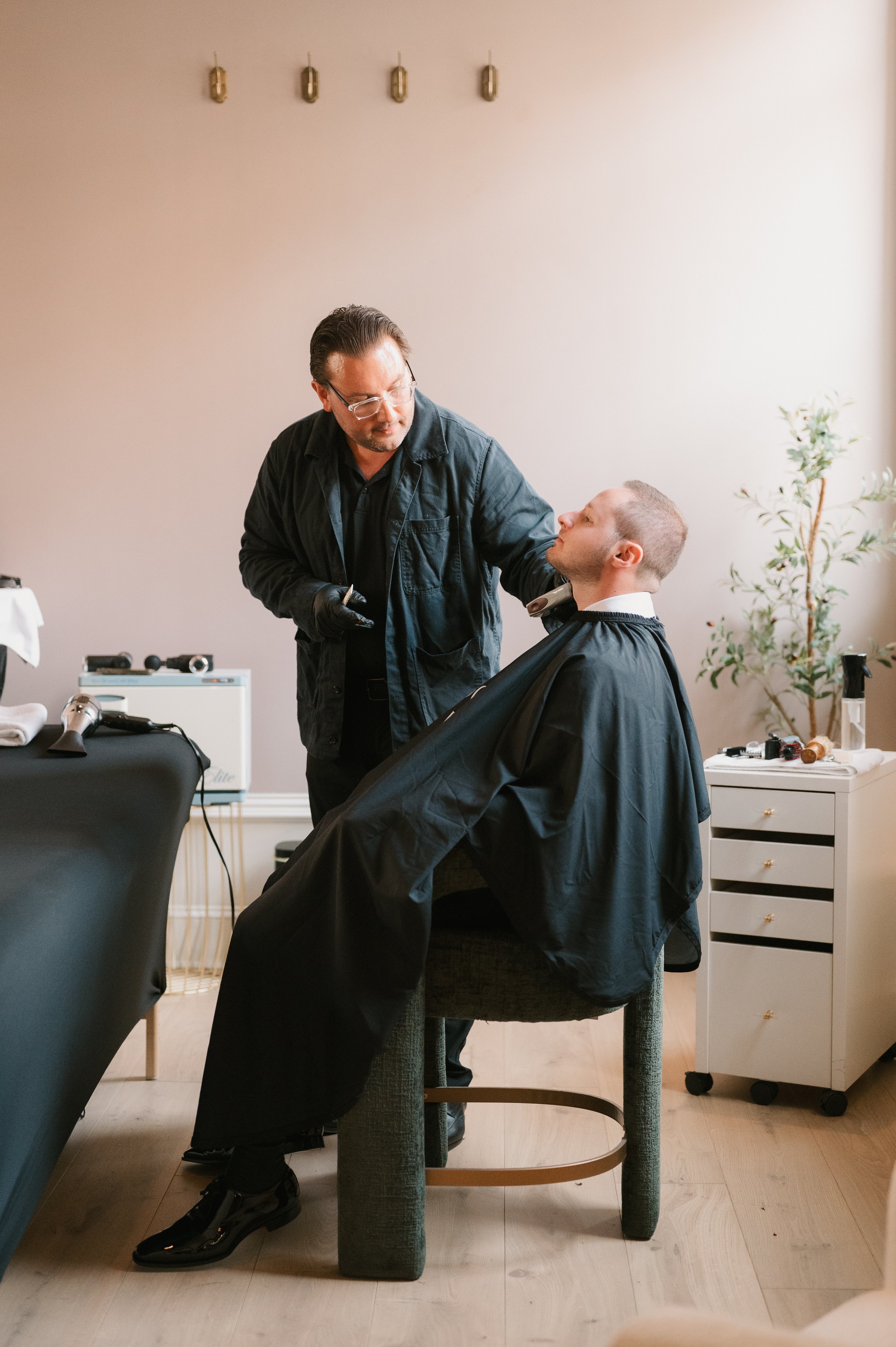Barber cutting a man's hair in a salon, with hair styling tools on a table nearby.