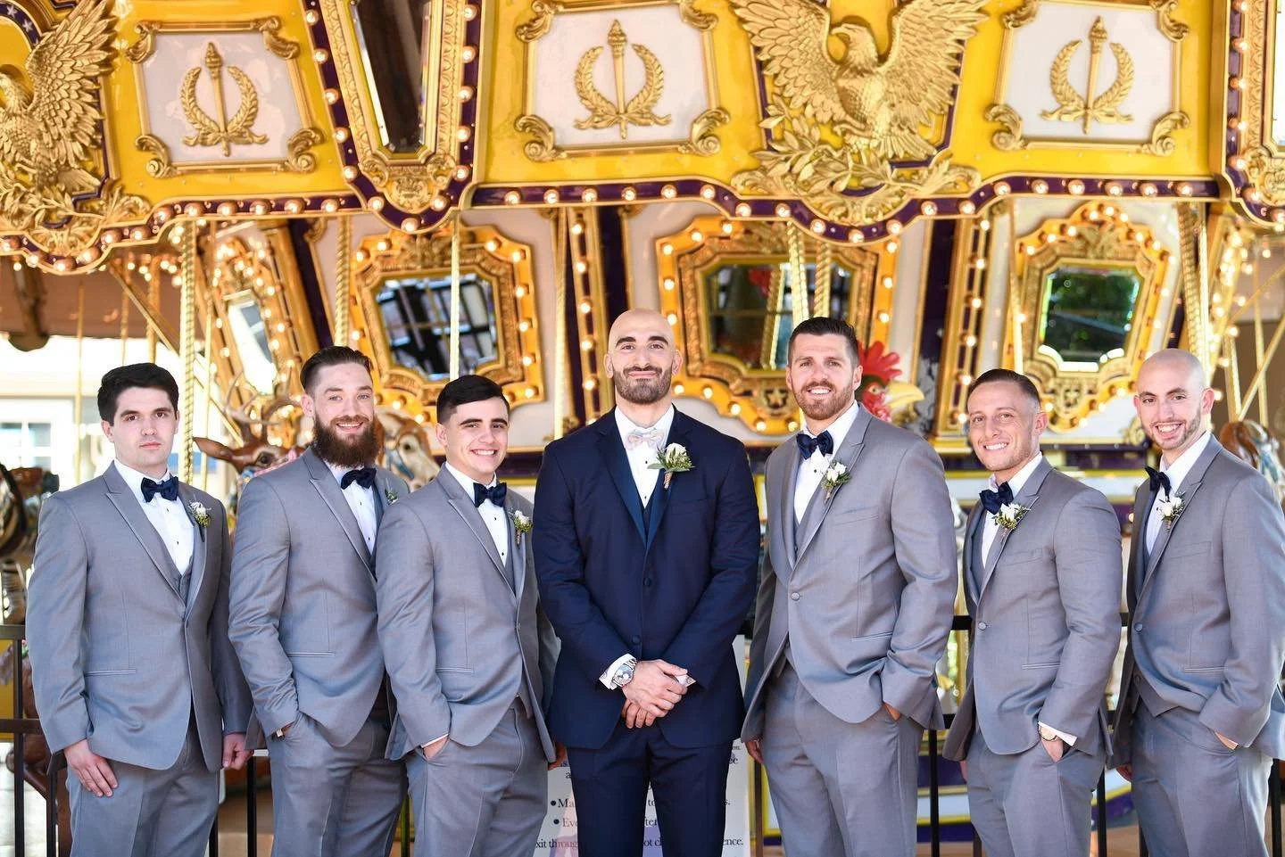 Groom and groomsmen in suits standing in front of a carousel.