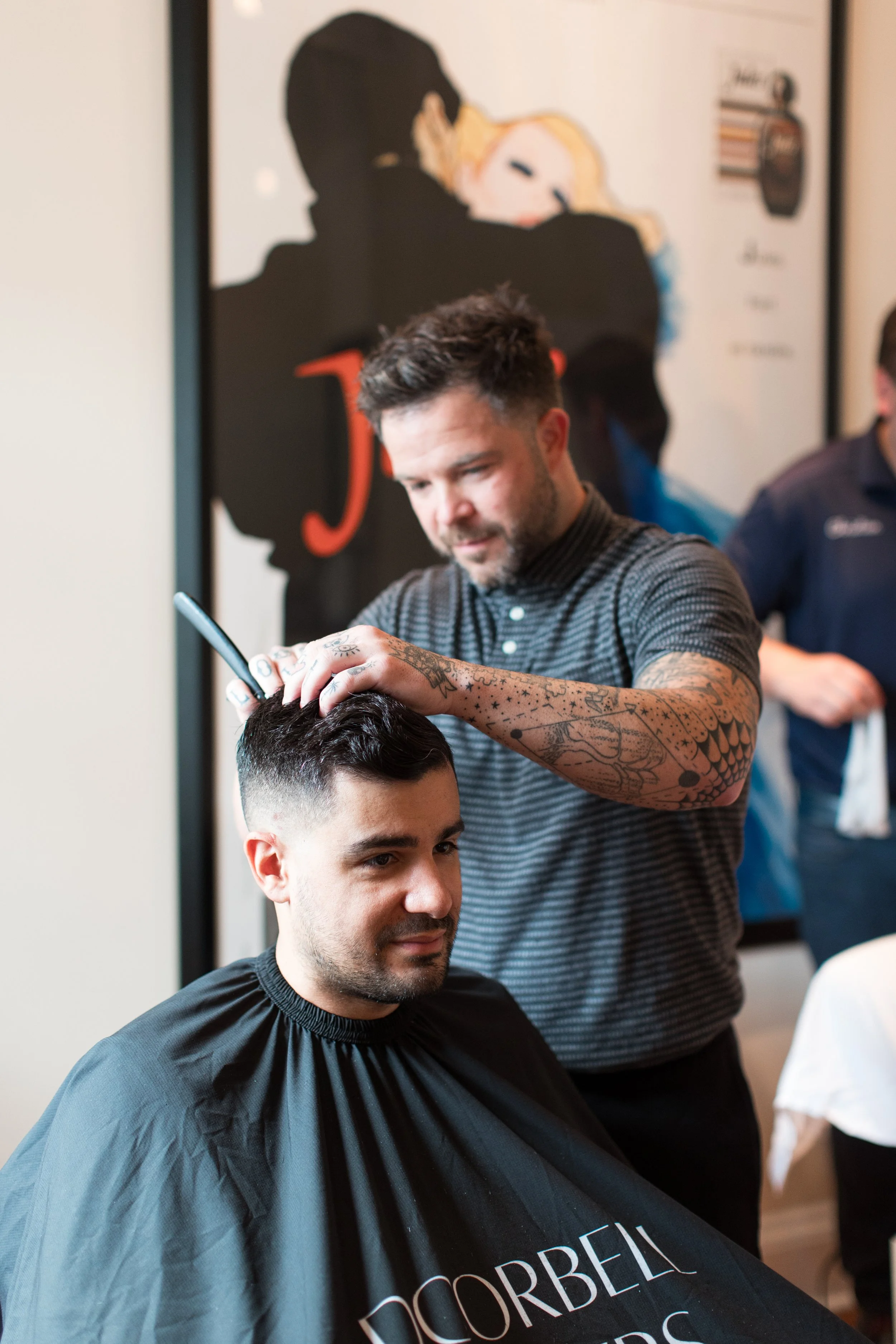 Barber giving a man a haircut with clippers in a salon, with a poster on the wall.