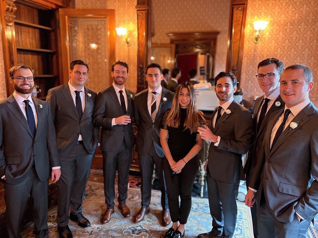 A group of people dressed formally in a room with elegant decor, including wood paneling and patterned wallpaper.