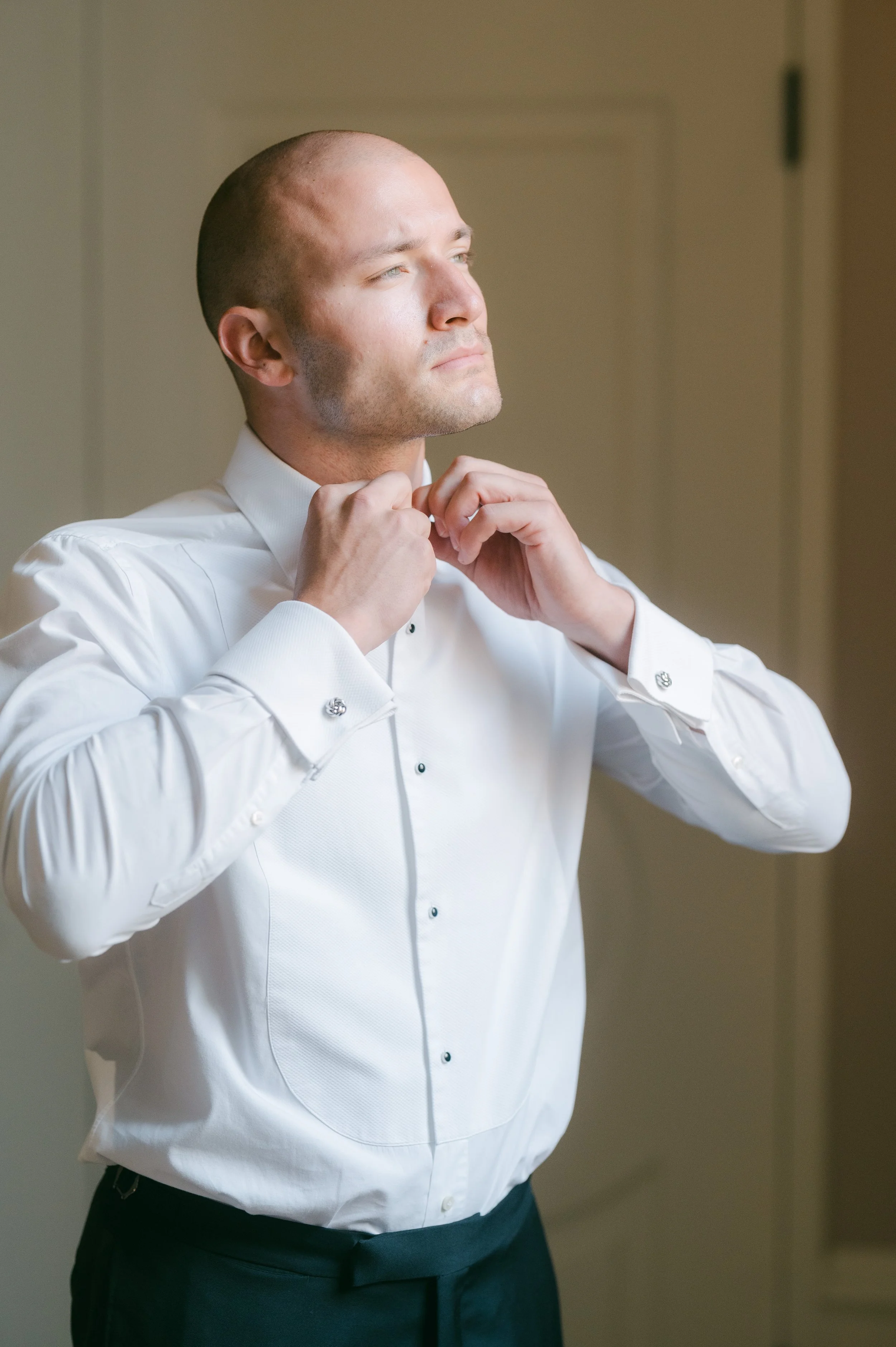 Man in white dress shirt adjusting his collar, preparing for a formal event.
