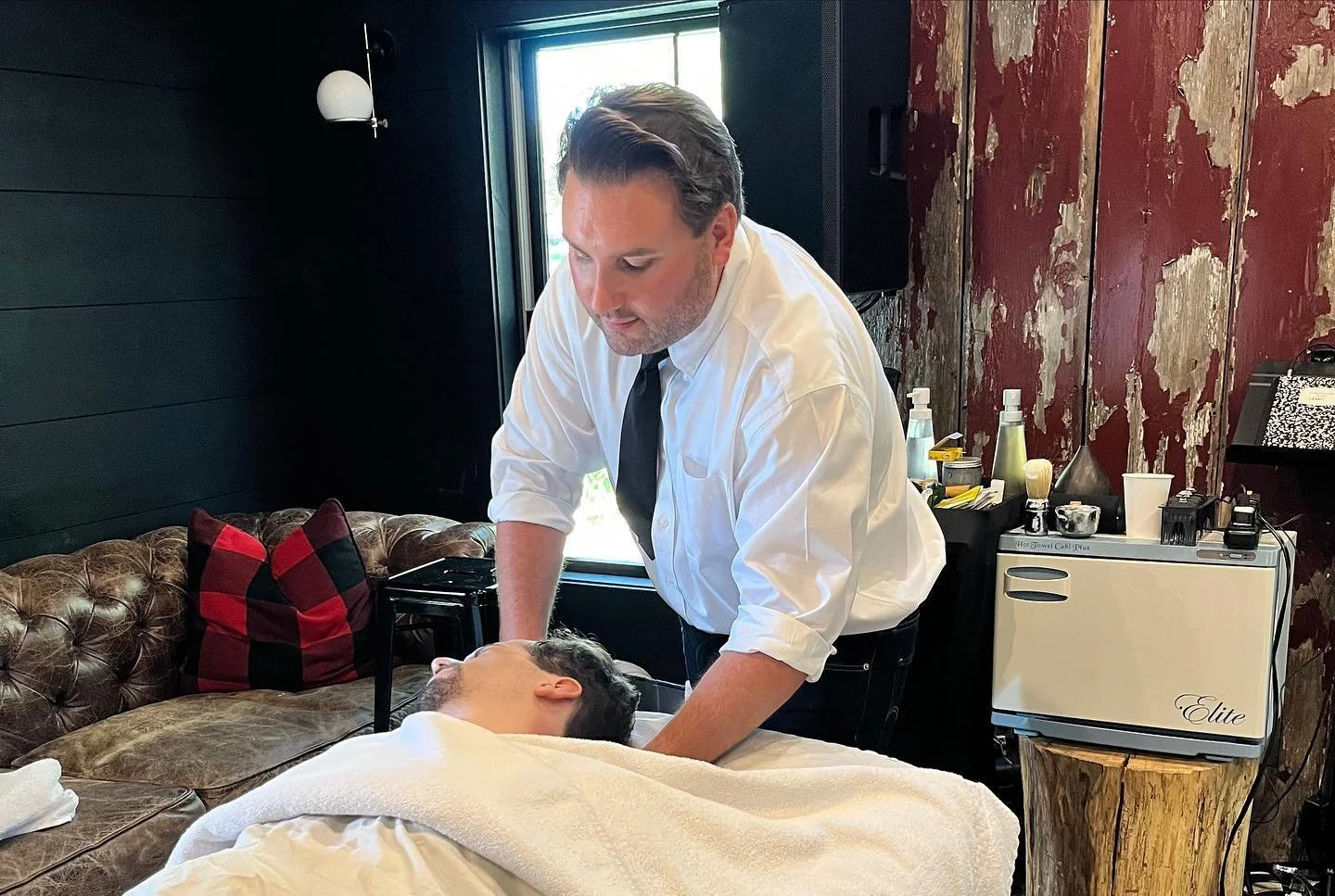 Man in white shirt giving a massage to another person lying face up on a massage table.