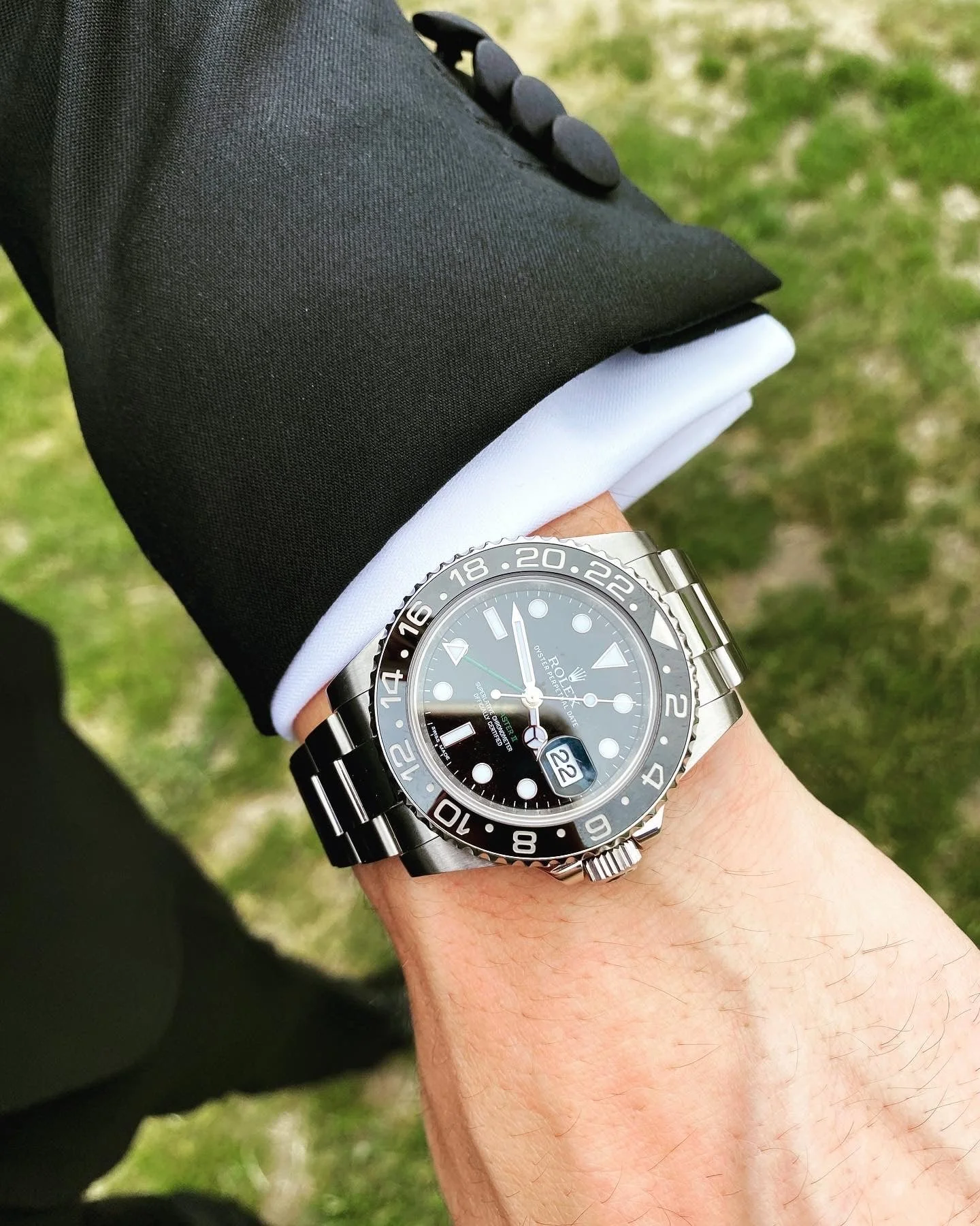 Close-up of a wrist wearing a luxury watch with black suit sleeve
