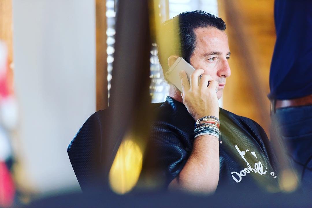 Man sitting indoors talking on a smartphone with bracelets on his wrist.