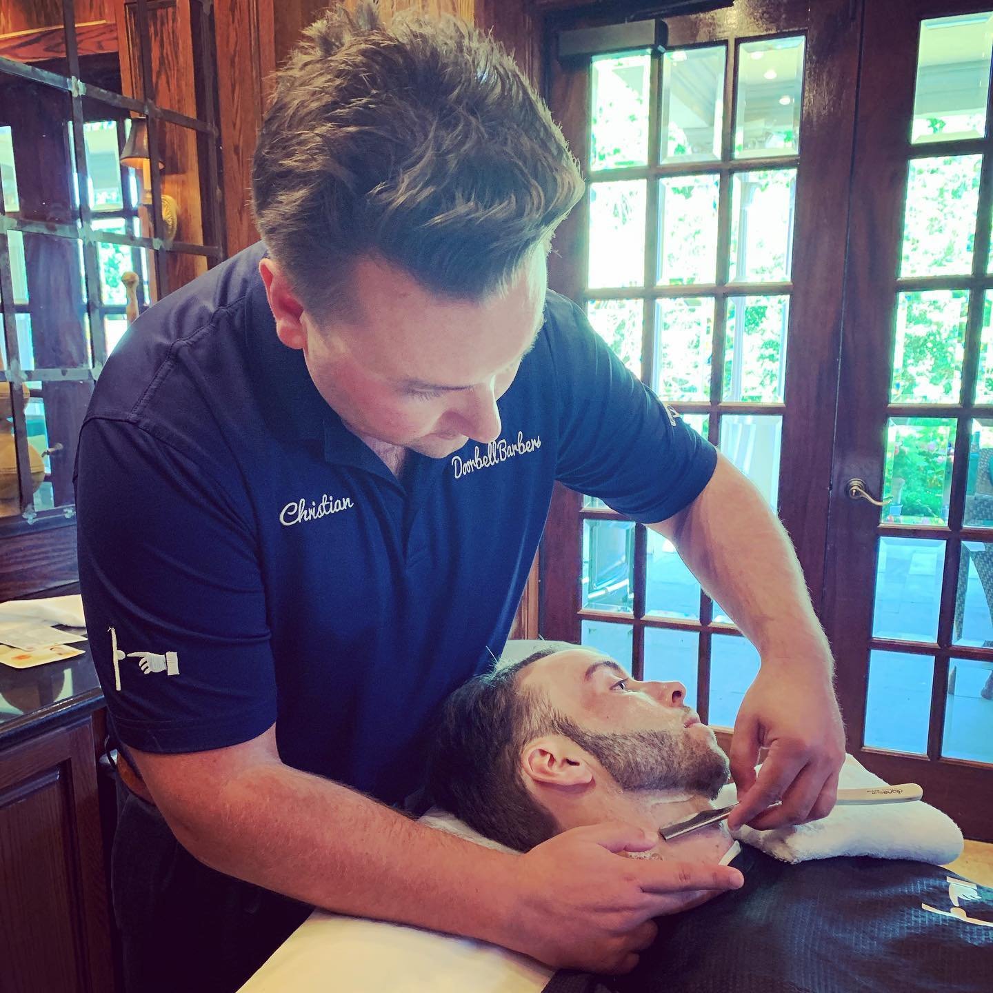 Barber shaving a man's beard with a straight razor in a barbershop.