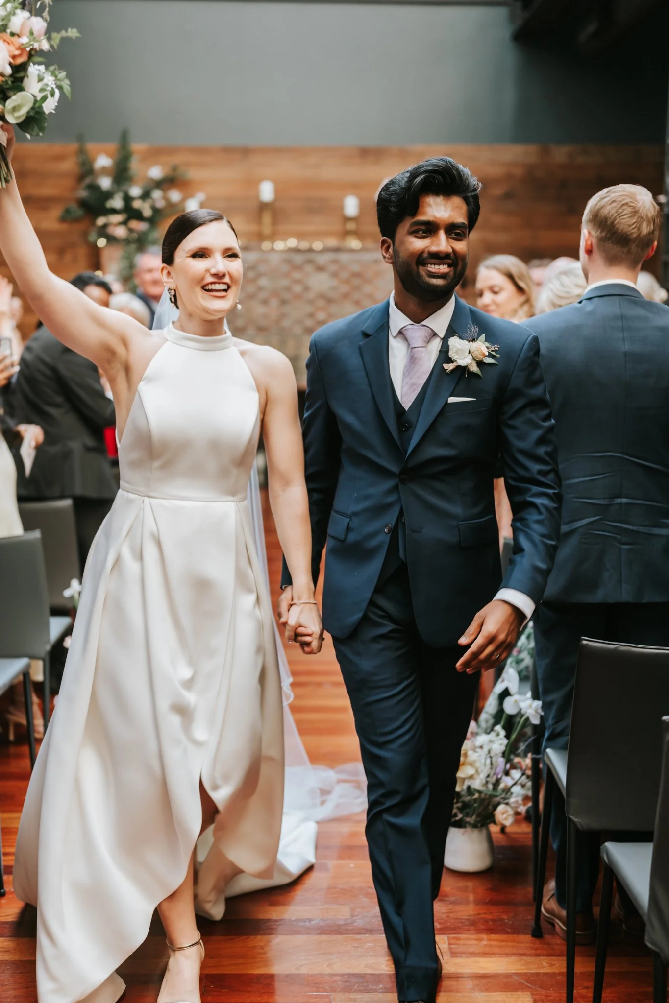 Bride and groom holding hands, smiling, walking down the aisle at a wedding ceremony.