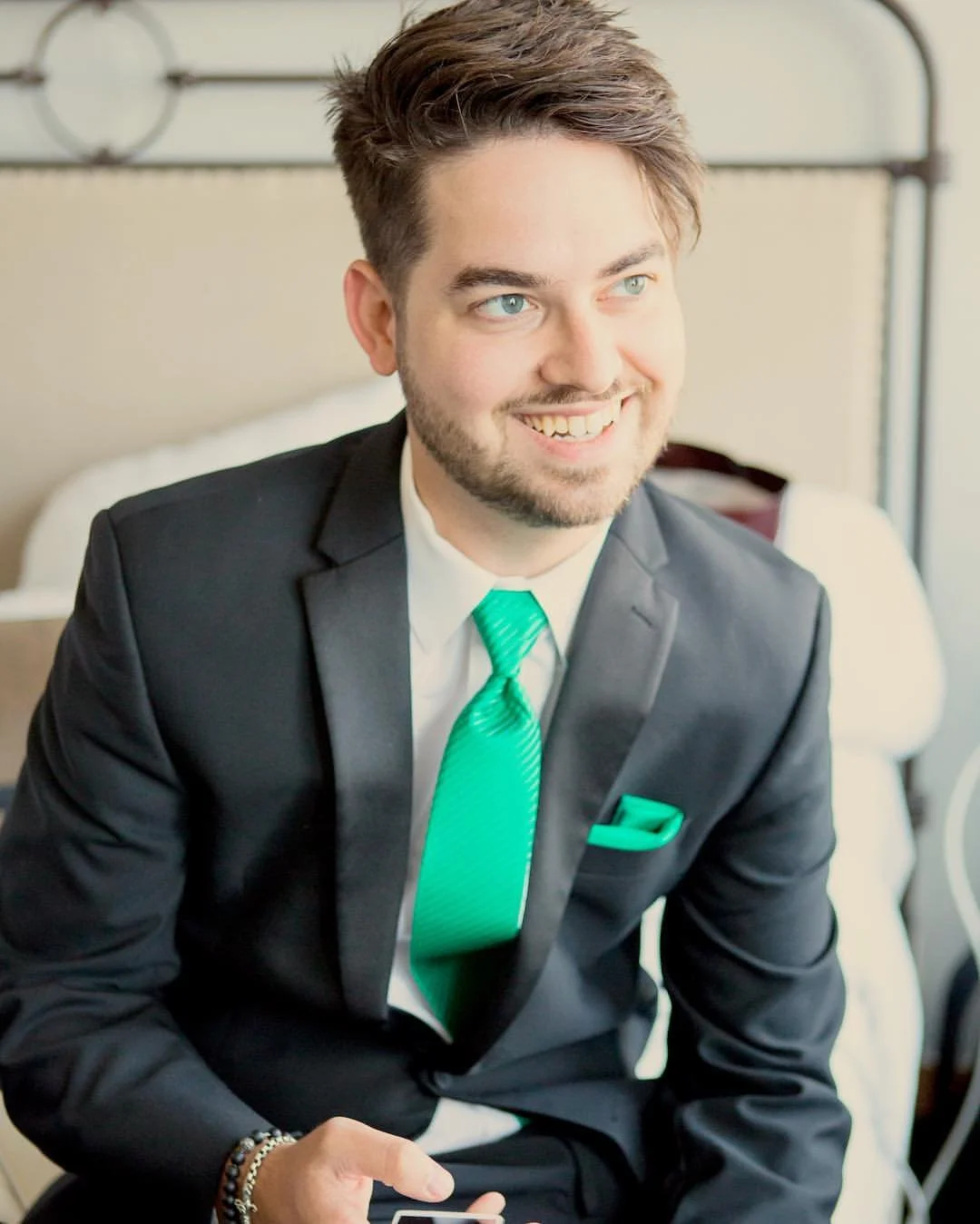 Man in a suit with a green tie and pocket square sitting and smiling