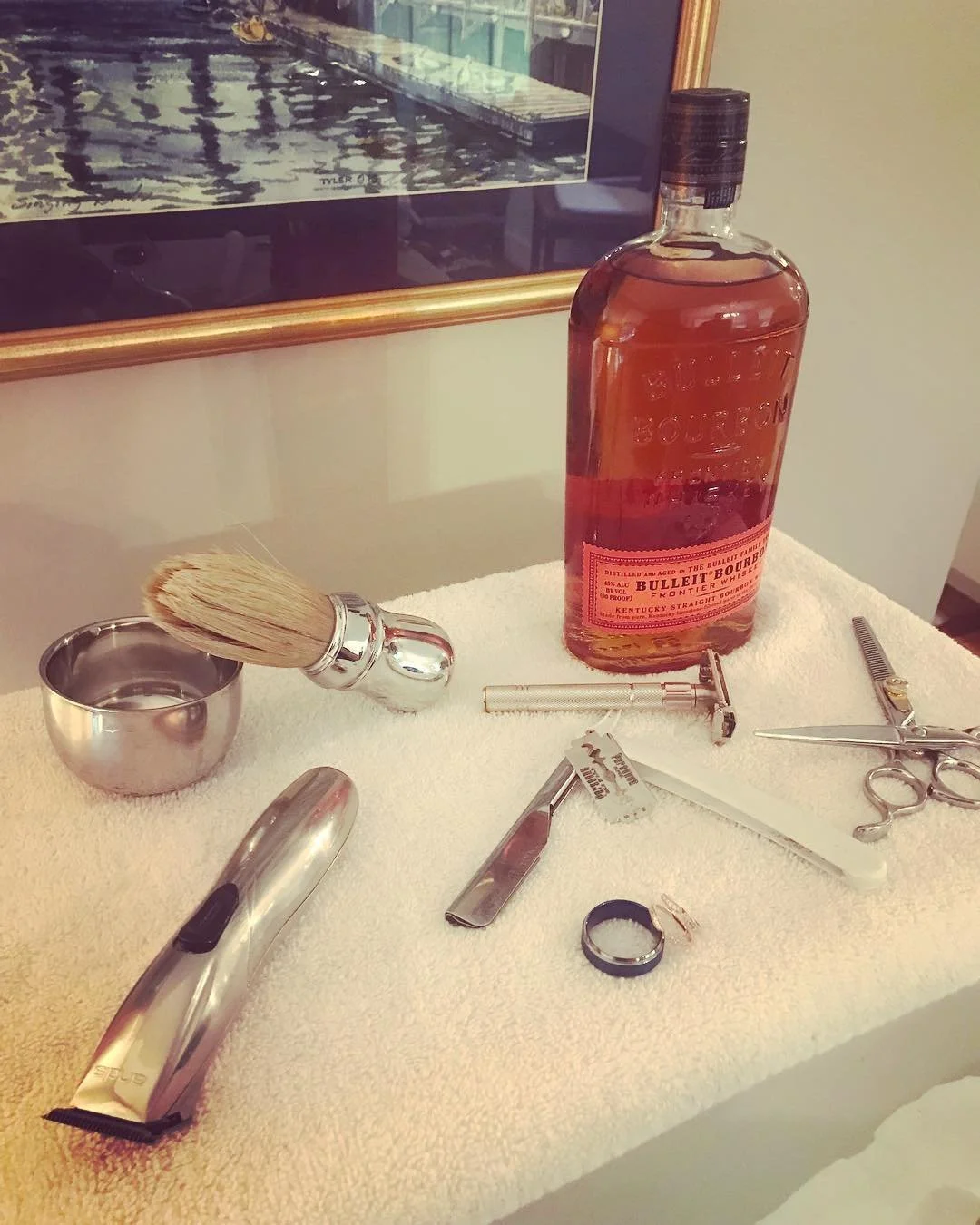 Shaving tools and Bulleit Bourbon bottle on white towel