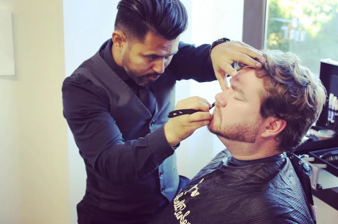 Makeup artist applying makeup to a seated man's face.