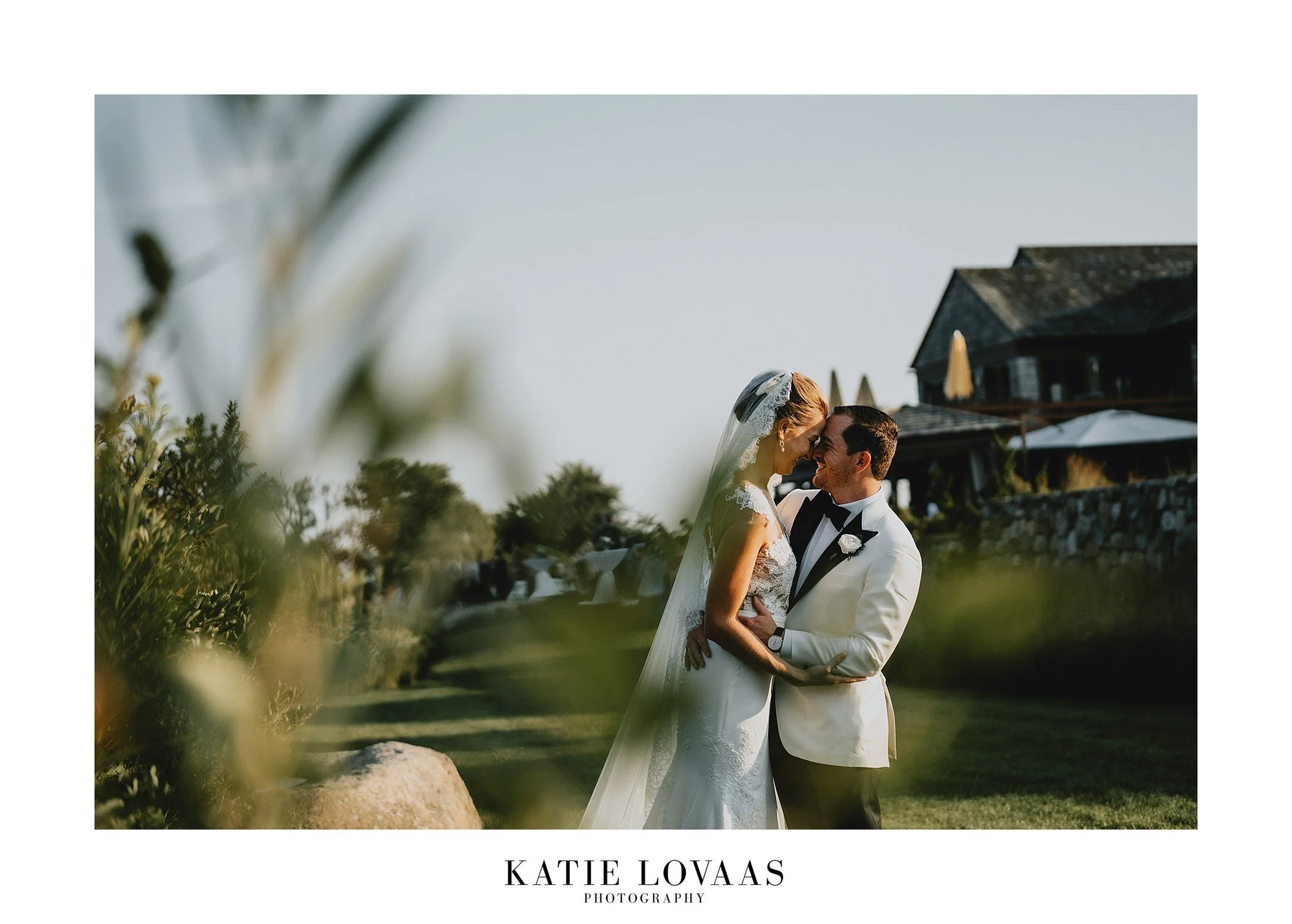 Bride and groom embracing outdoors with a scenic backdrop, wearing a white wedding dress and a white tuxedo.