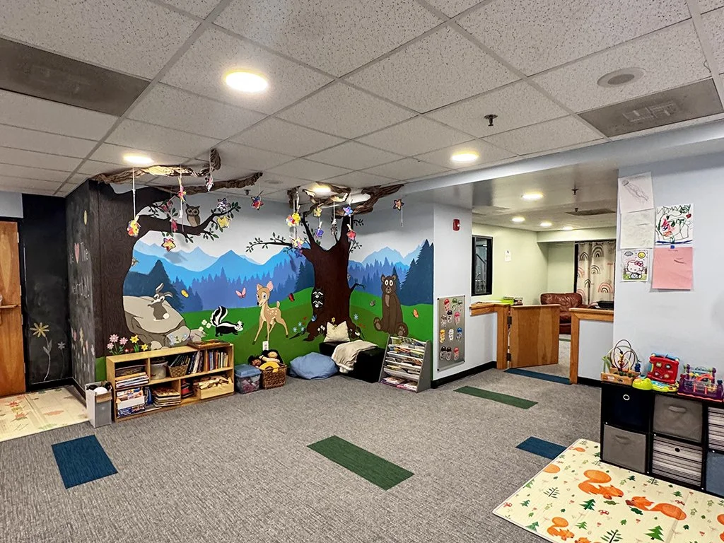 A colorful children's playroom with a forest-themed mural covering one wall.