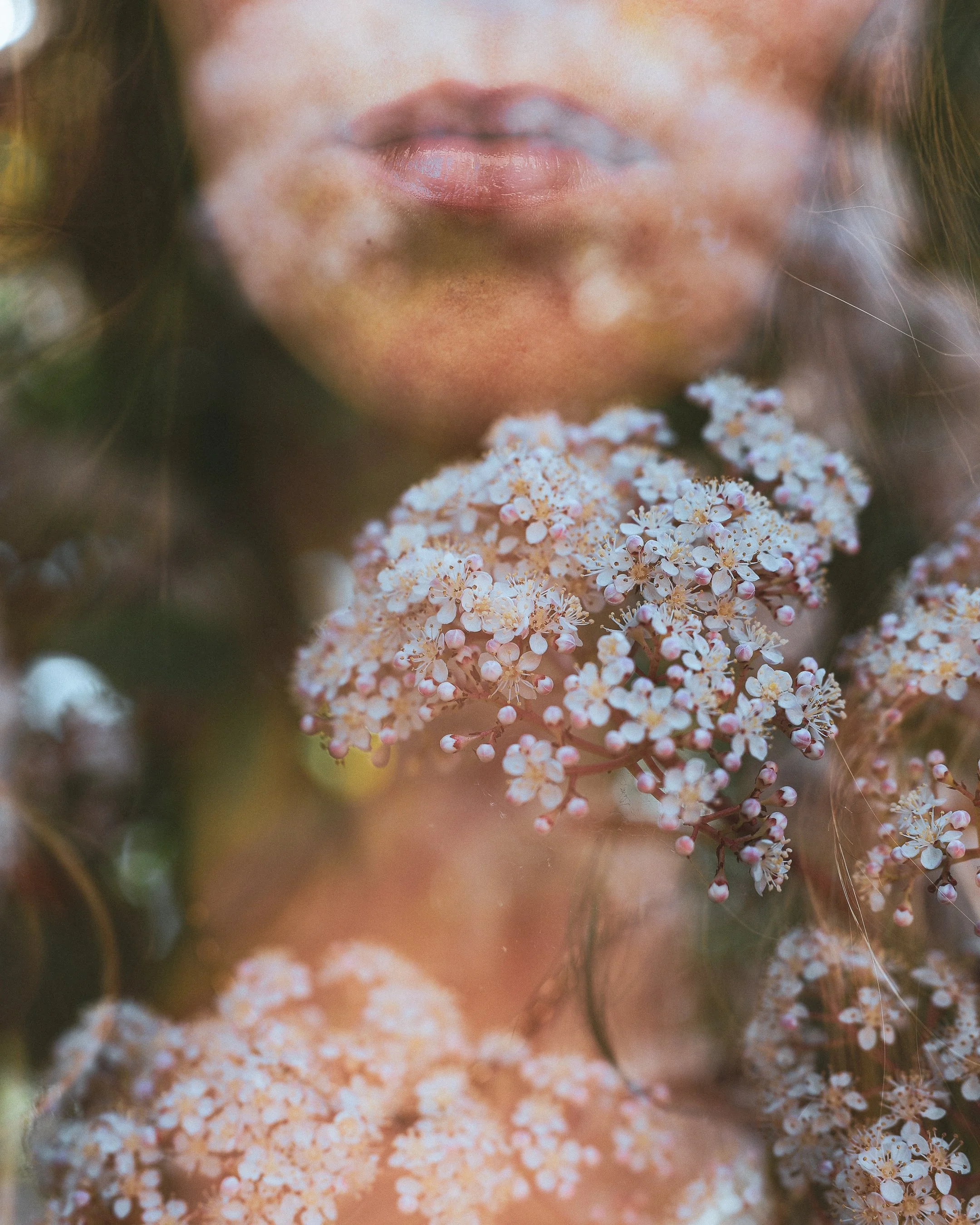 A close-up of a woman's face with her lips slightly parted, surrounded by white and pink flowers, with soft lighting.