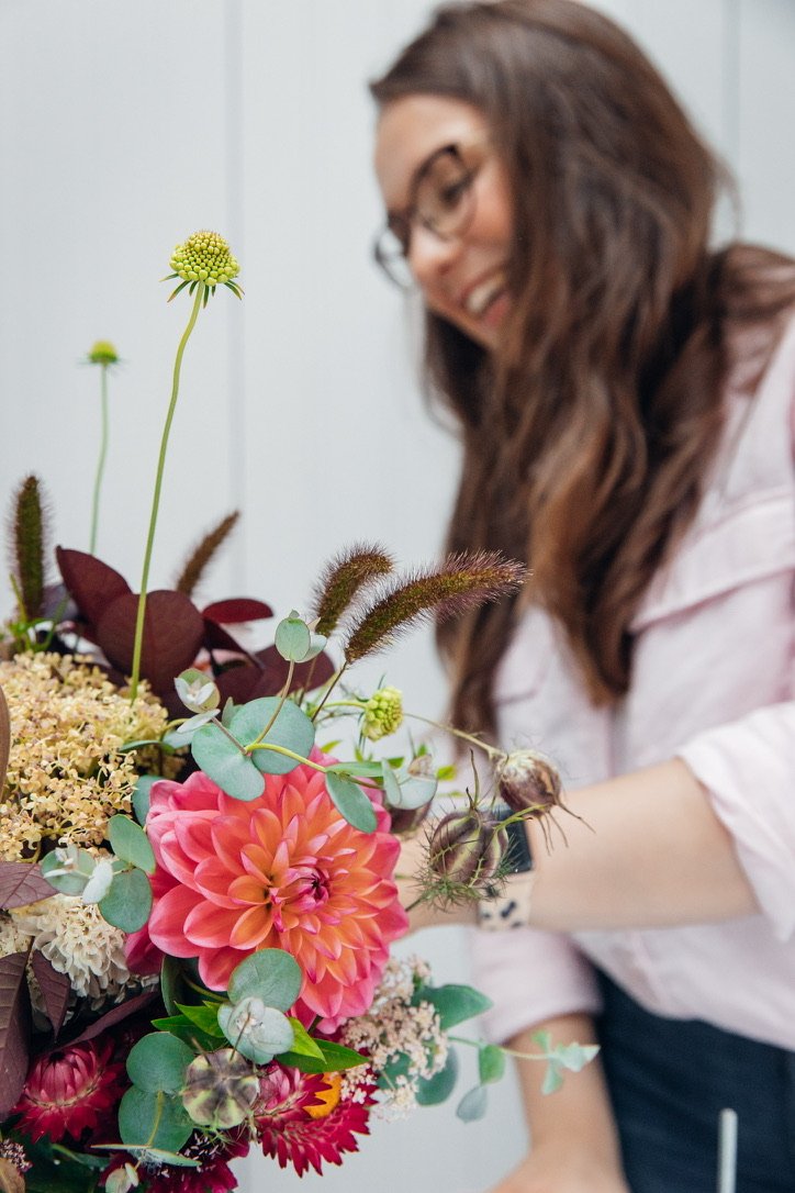 An image of Lucy smiling in the background with a bouquet of flowers in focus in the foreground