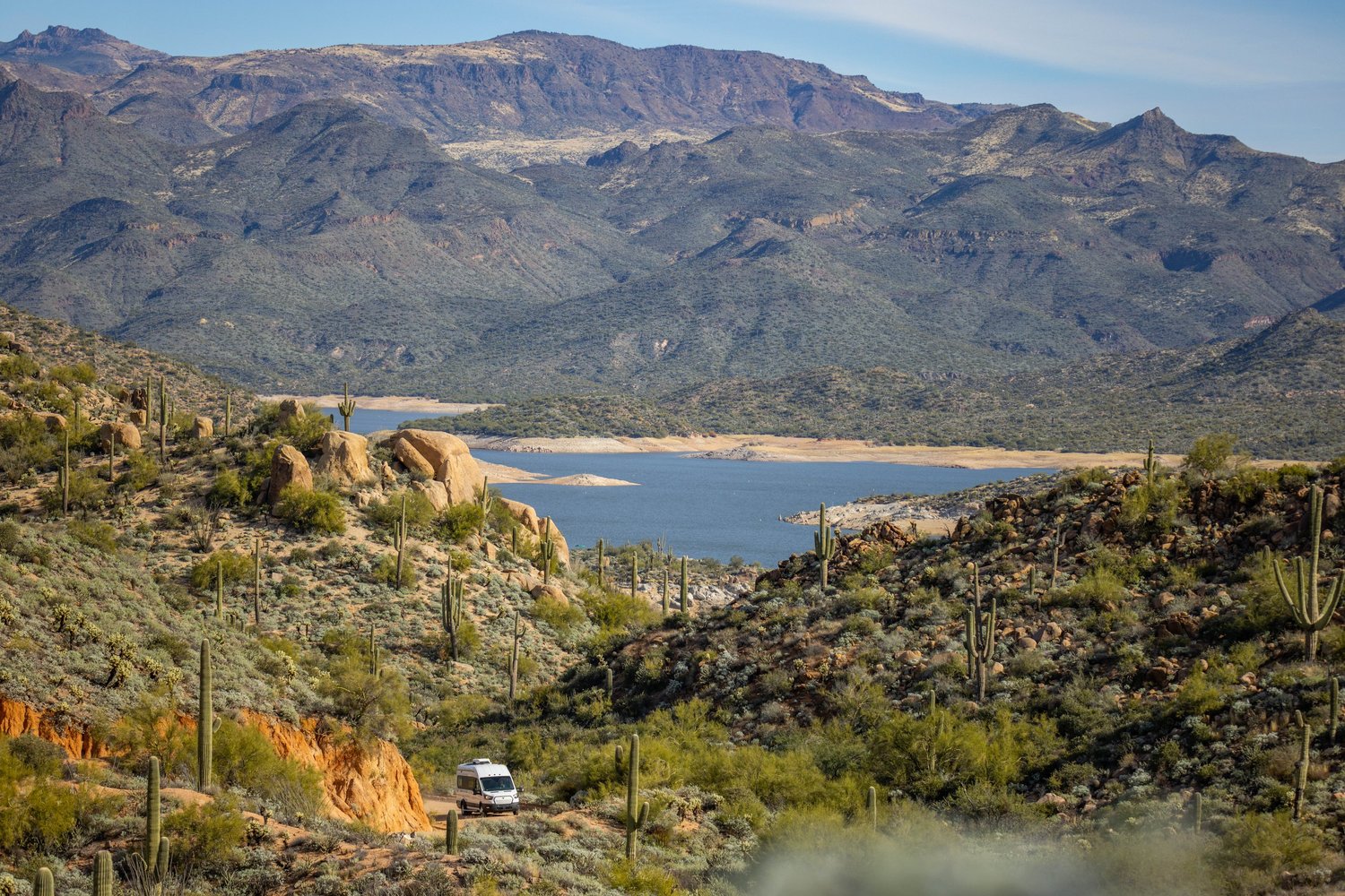 A desert landscape with cacti, a river, mountains, and a small camper van.