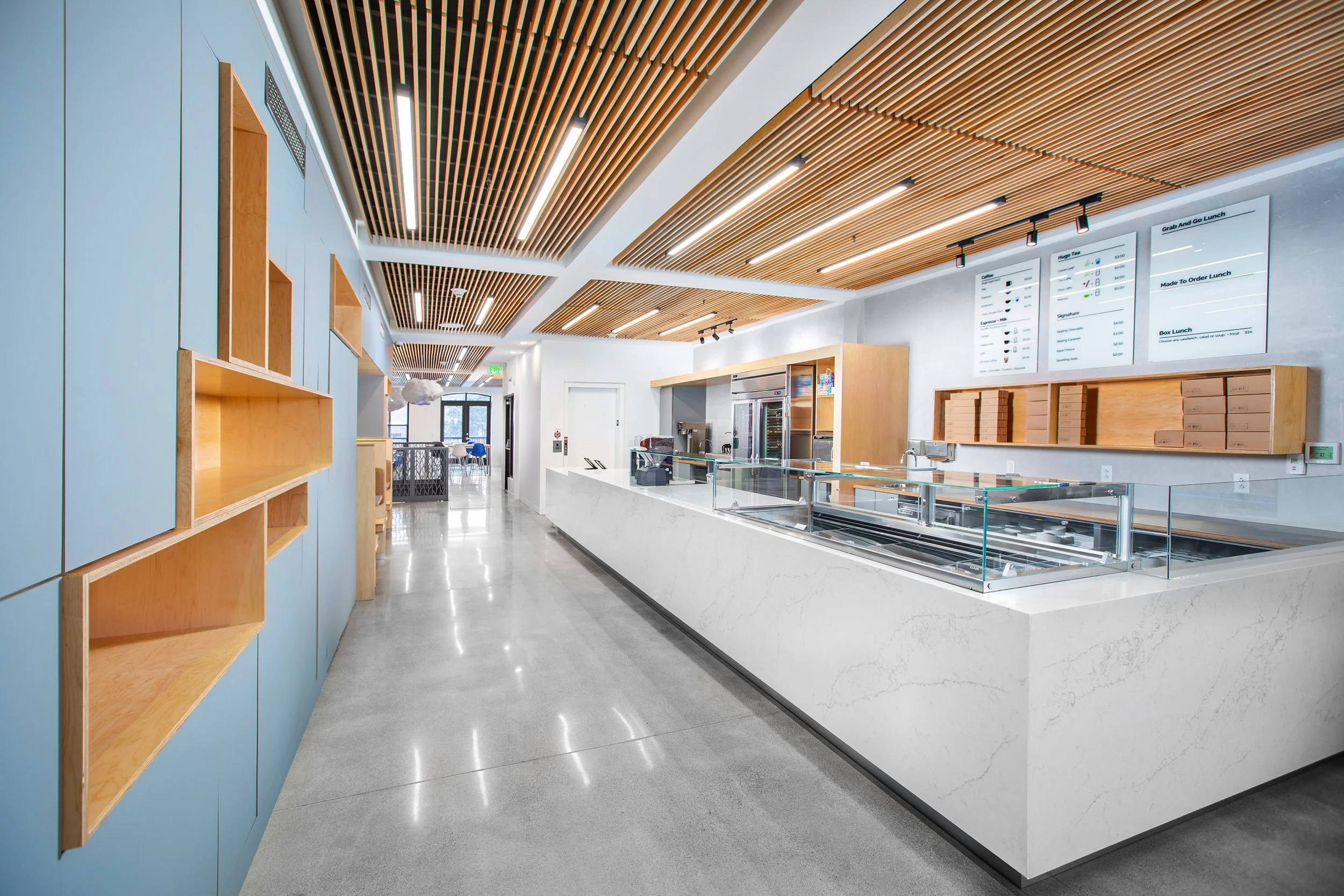 Modern restaurant counter with digital menu boards, blue and wood accents, and seating area in the background.