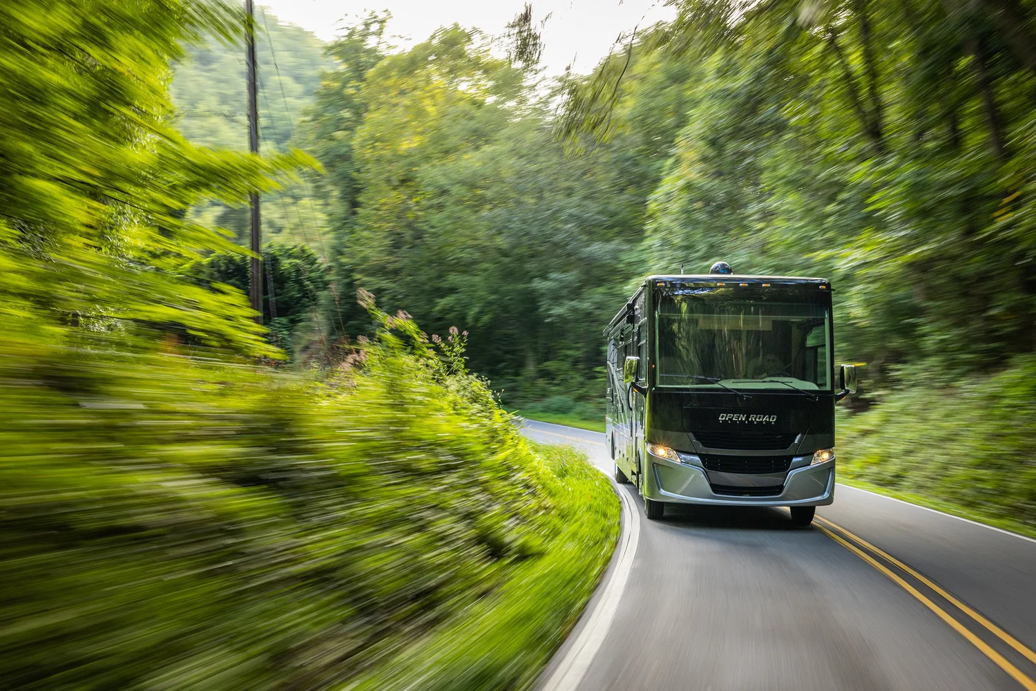 A black recreational vehicle driving along a winding forest road with motion blur of trees and greenery on both sides.