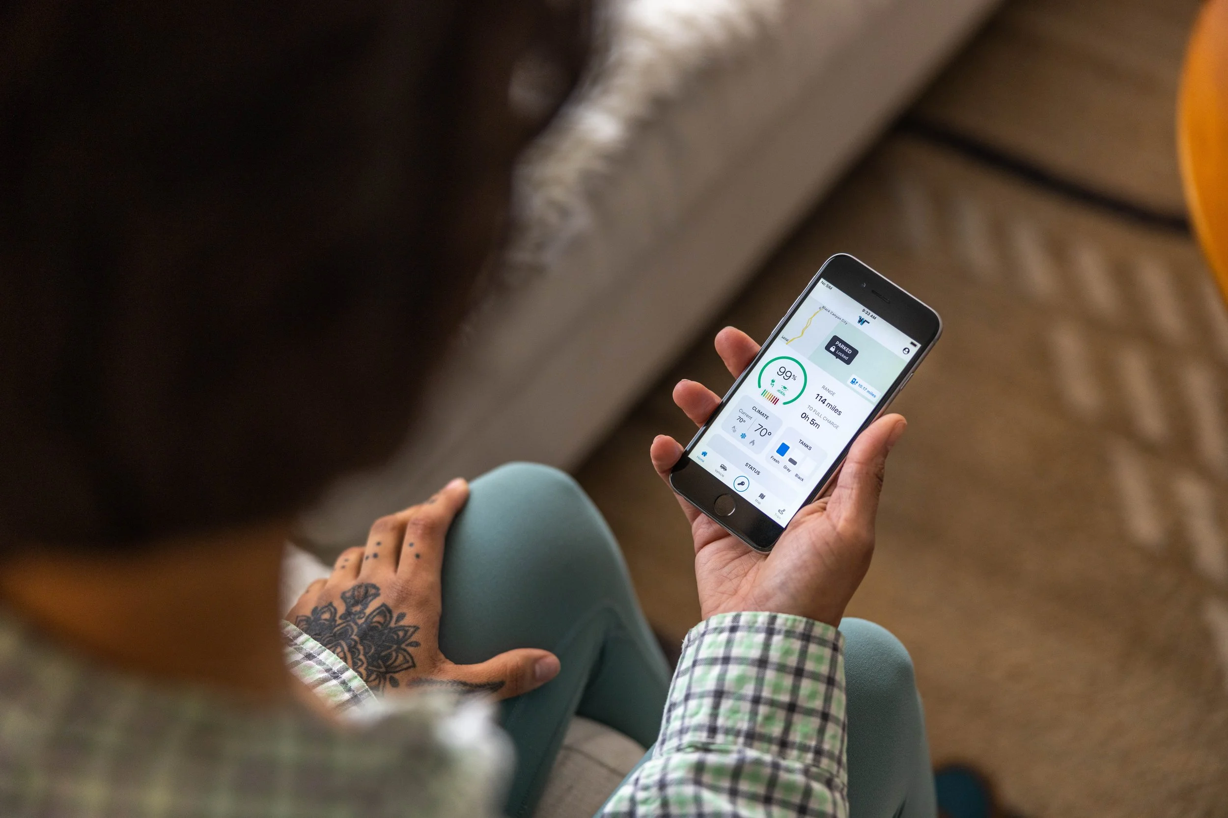 Person holding a smartphone displaying a health app with details such as 90% charge, 114 miles remaining, and 70°F temperature.