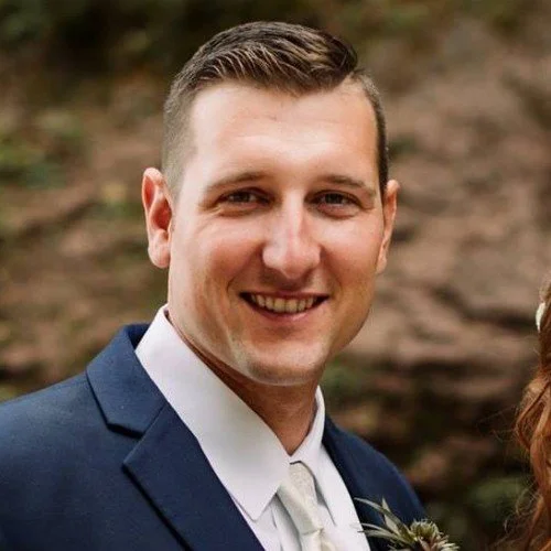Close-up of a smiling man in a navy suit and white shirt outdoors