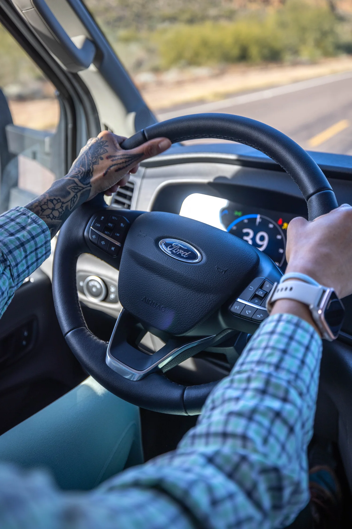 Interior view of a vehicle dashboard showing hands on the steering wheel, with a digital speedometer reading 39 mph.