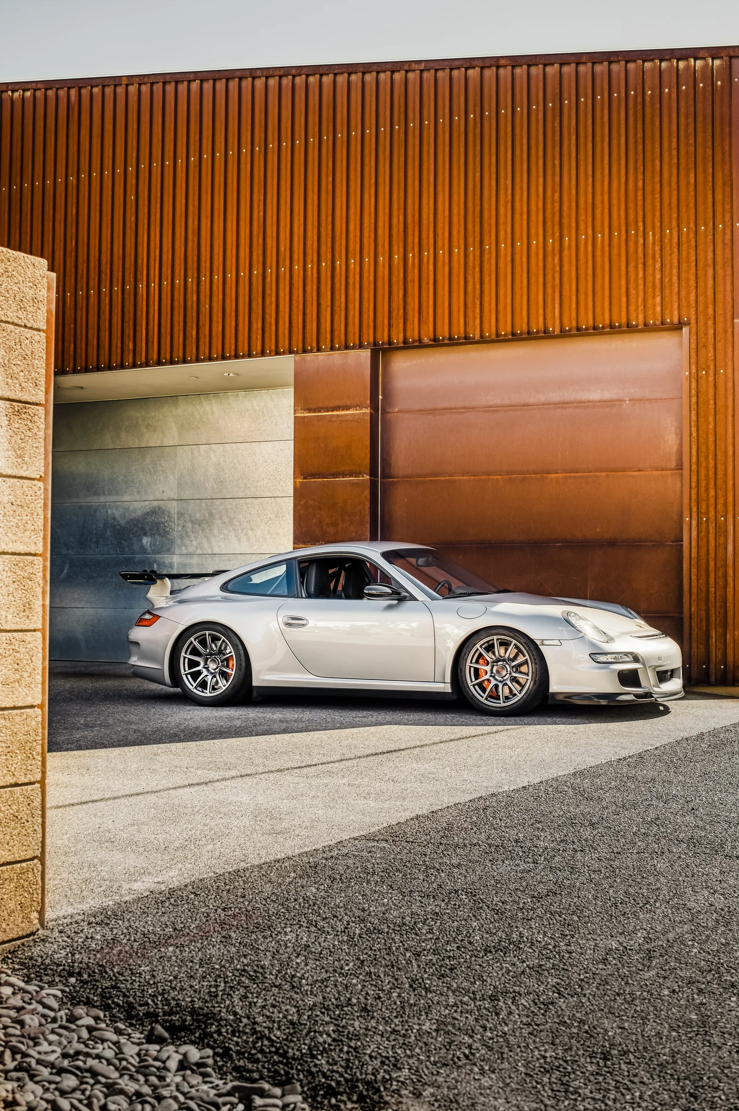 Silver sports car parked in front of modern architectural building with wooden and metal panels.