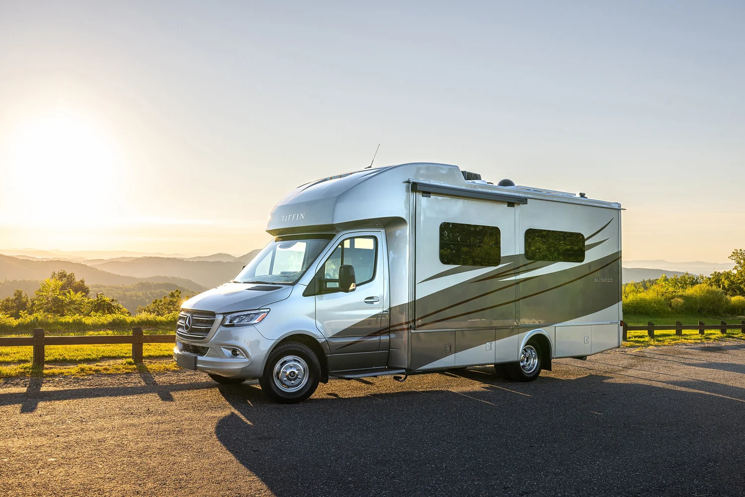 Silver camper van parked on the side of the road with mountains and a sunset in the background.