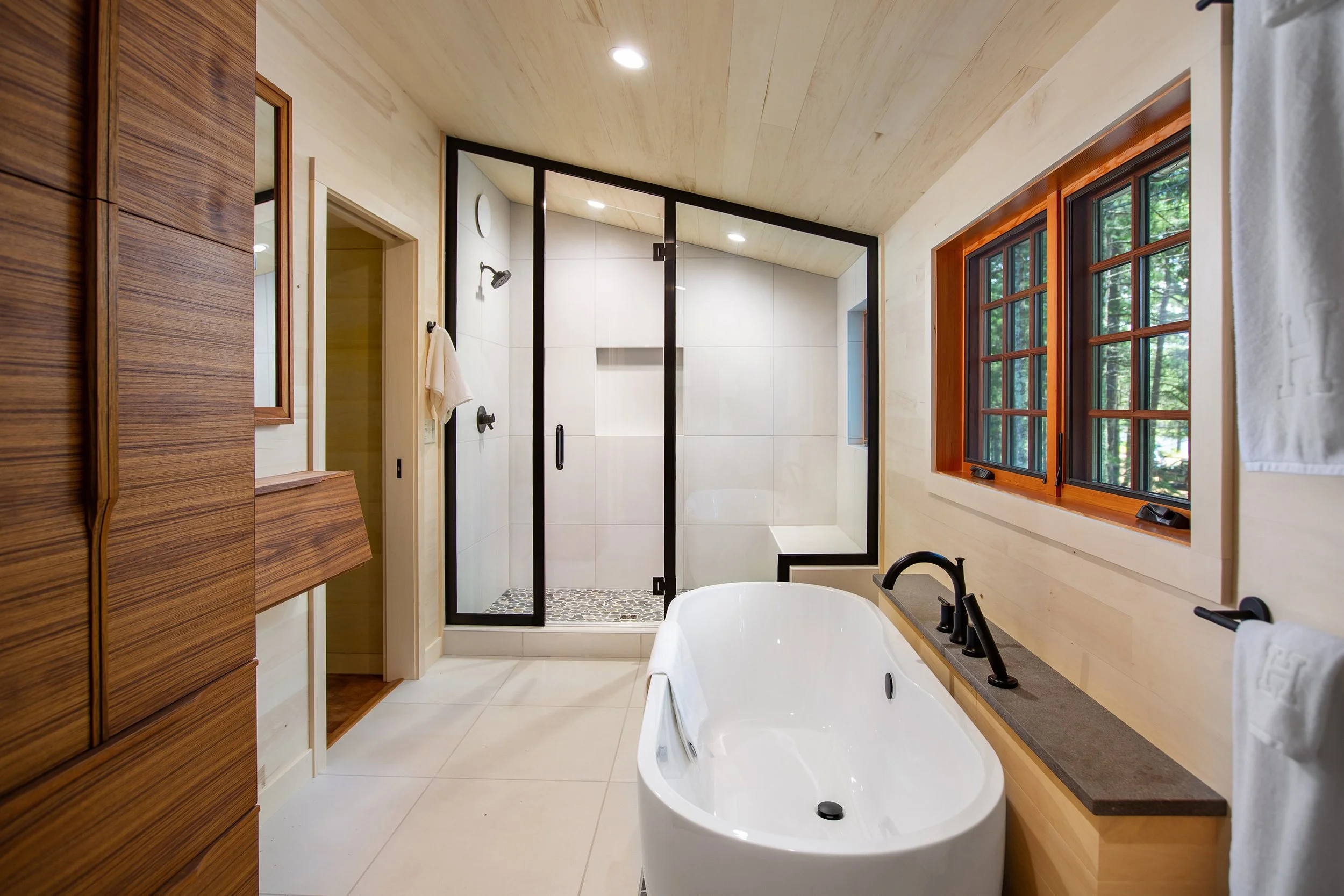 Modern bathroom with a bathtub, a large window, and a walk-in shower with a glass door.