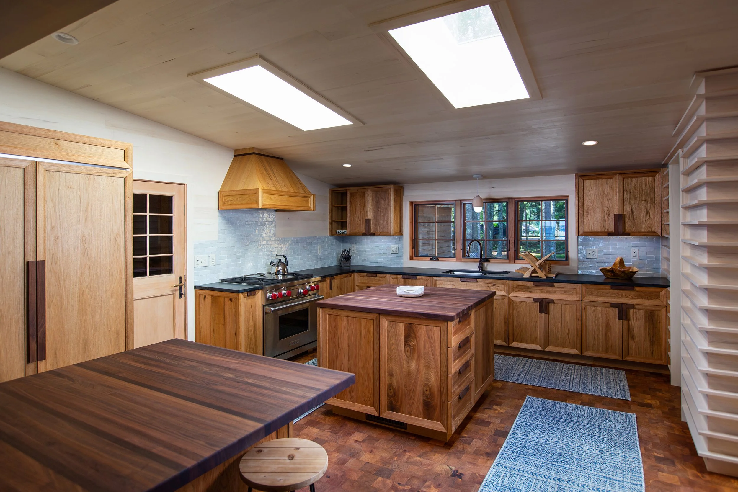 Kitchen with wooden cabinets, black countertops, a central kitchen island, a stainless steel oven, and windows overlooking trees.