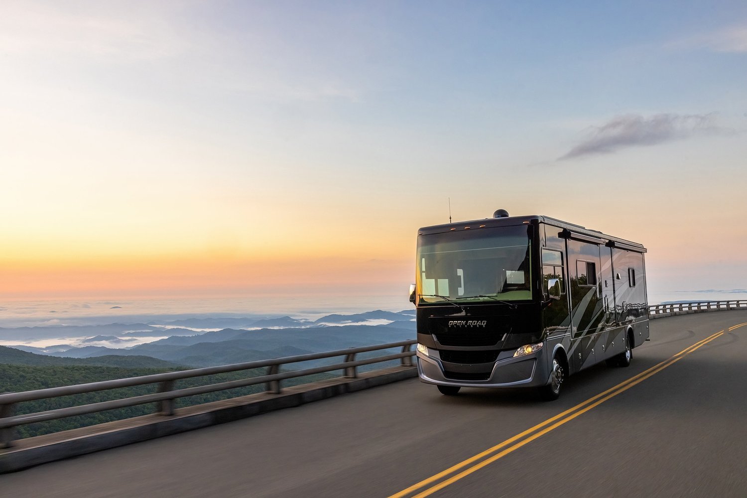 A black RV driving on a mountain road during sunset with cloudy sky and scenic mountain views in the background.