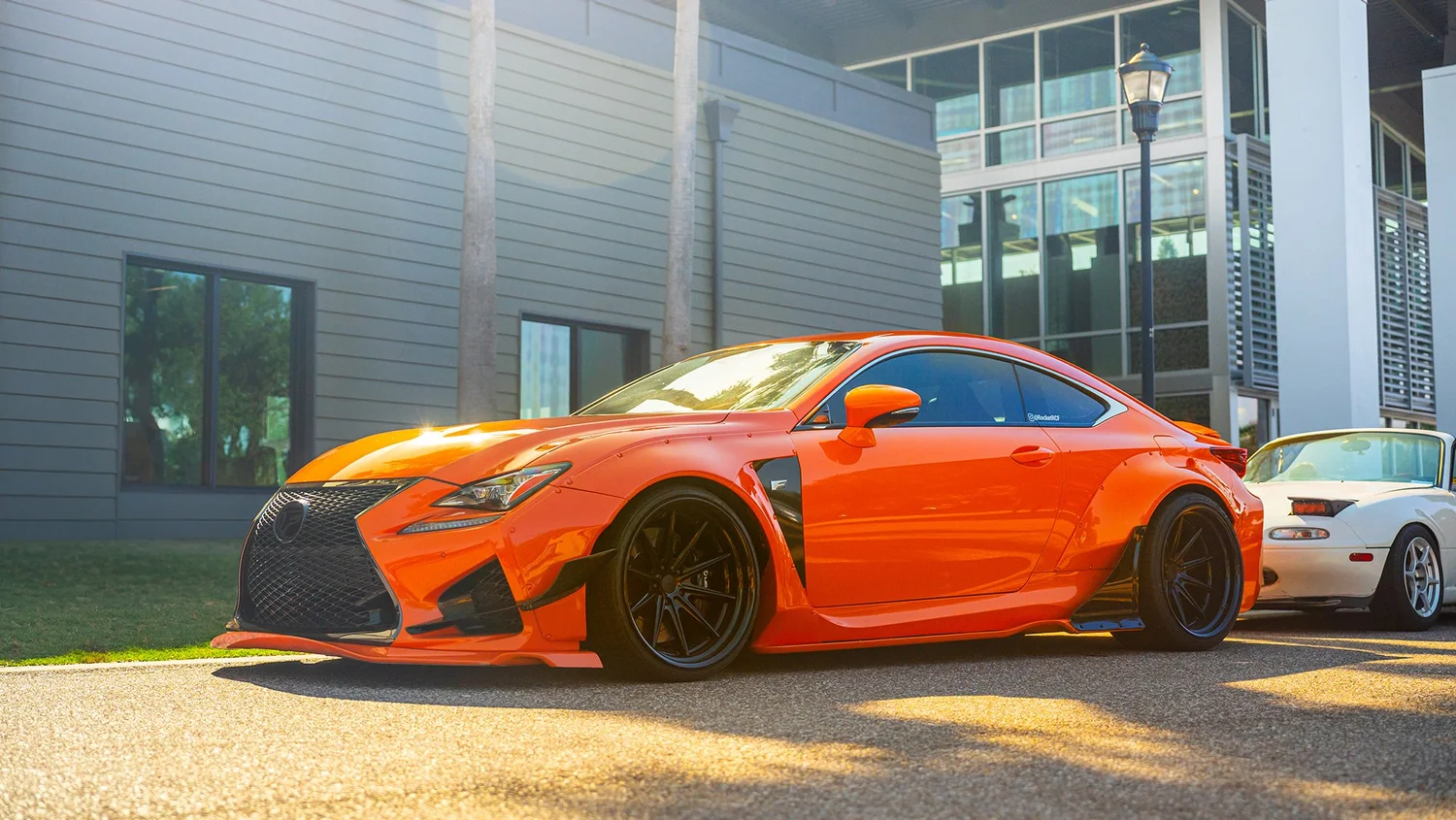 Orange sports car parked beside a white vintage car on a street in front of modern buildings.