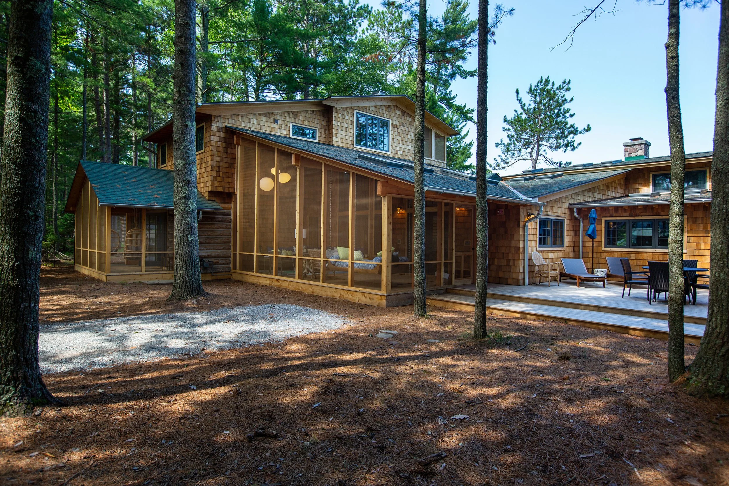A modern house with a screened porch and outdoor deck surrounded by trees in a wooded area.
