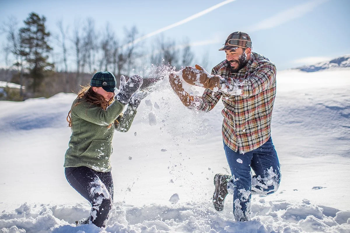 Man and woman playing in the snow, throwing snow at each other, outdoors on a sunny winter day.