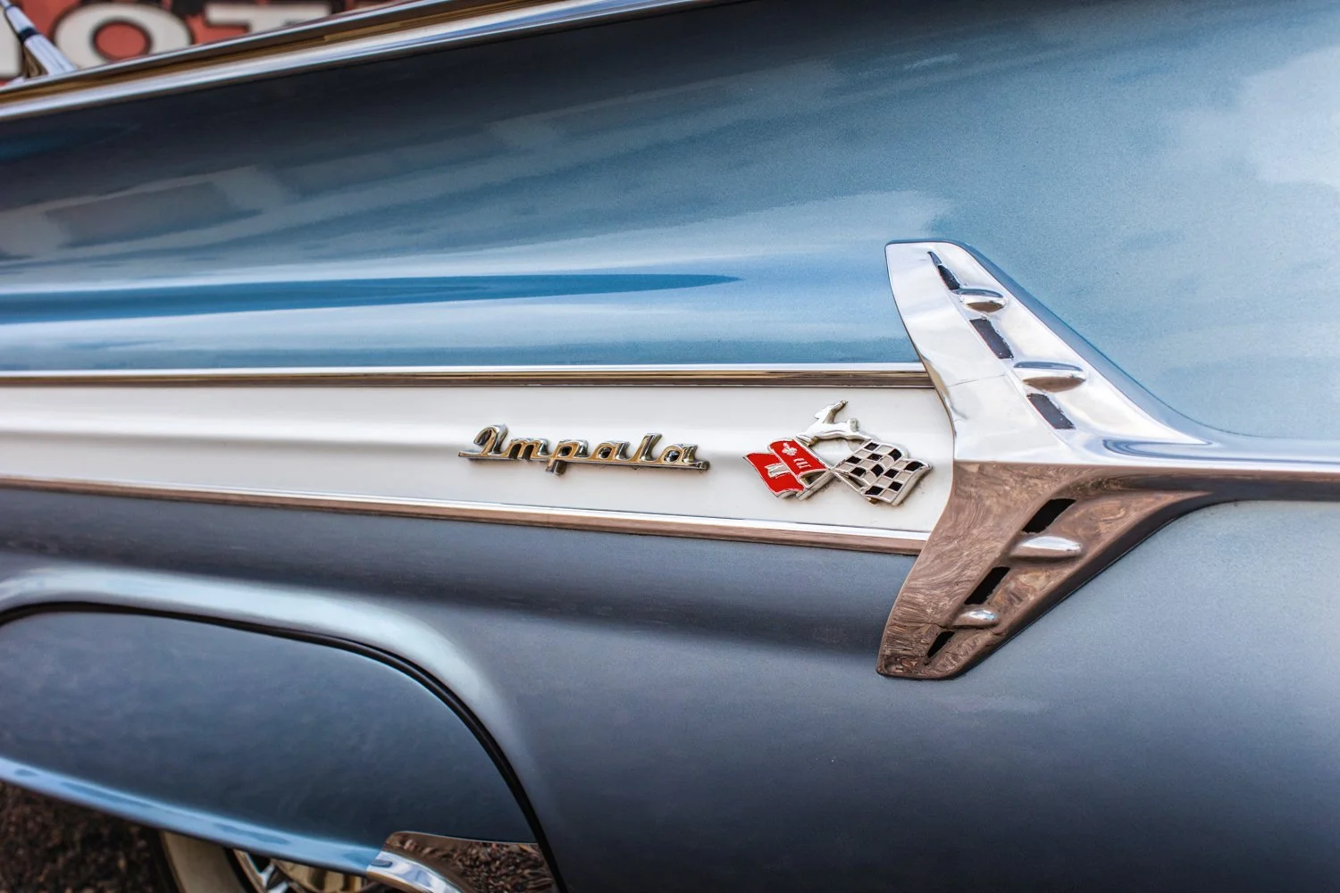 Close-up of the rear side of a vintage Chevrolet Impala, showing the Impala emblem and crossed flags badge on the blue and chrome body.