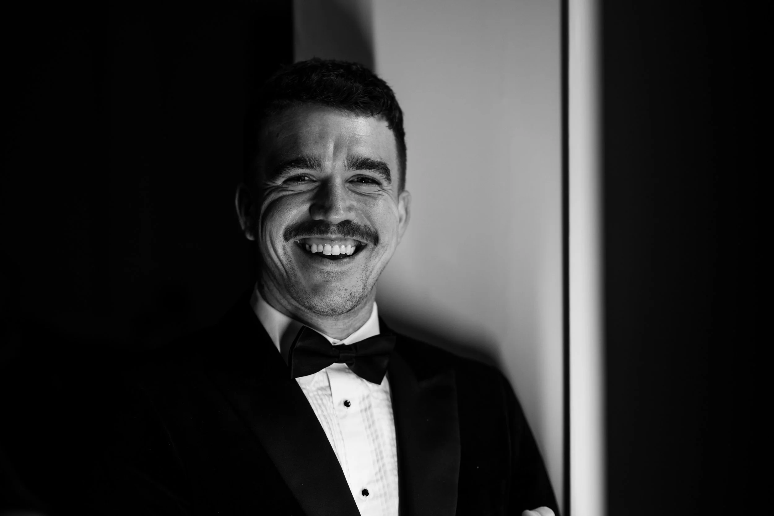 A man in a tuxedo smiling for a black and white photo.