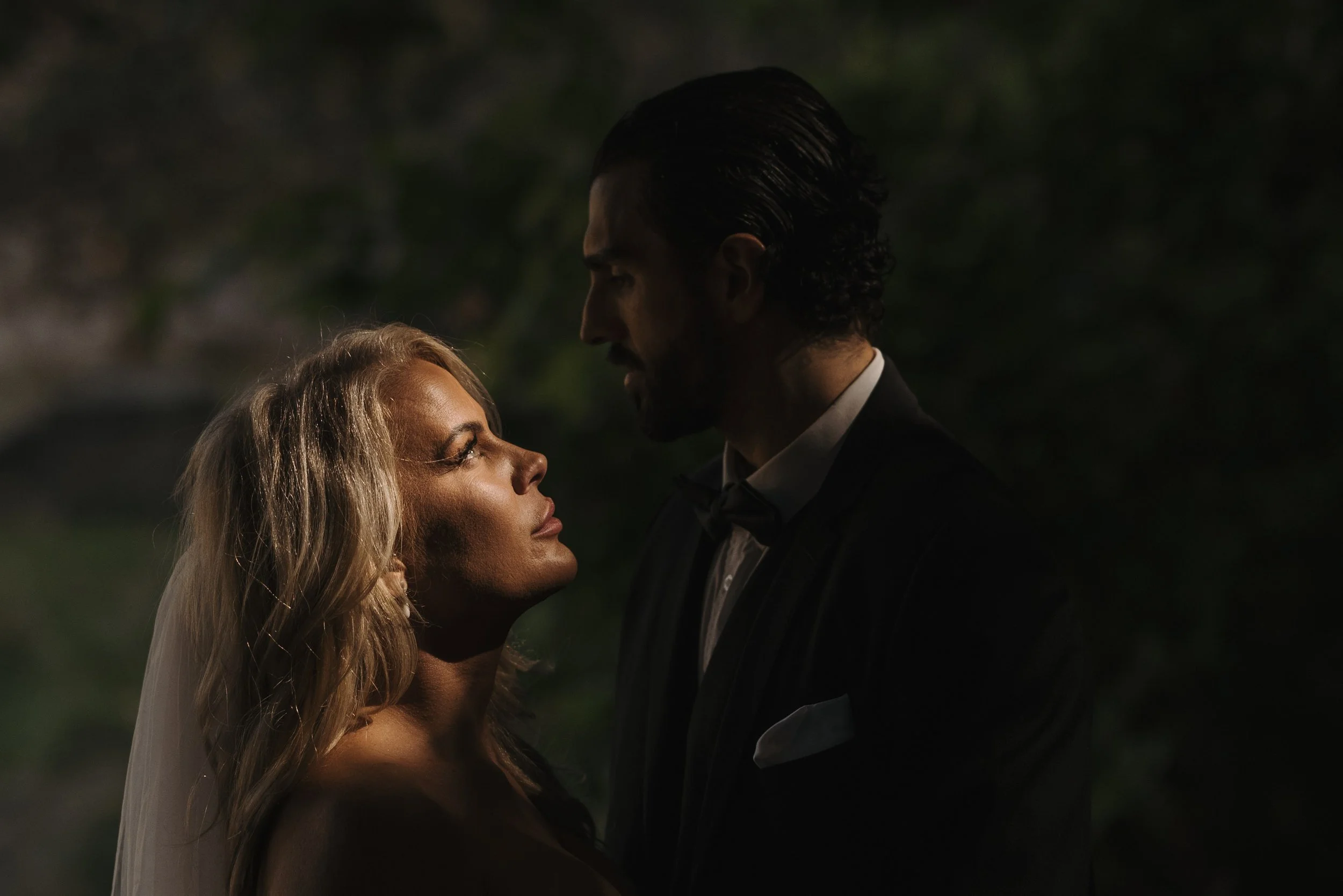 A man and woman gazing into each other's eyes at night, outdoors, with dark background.