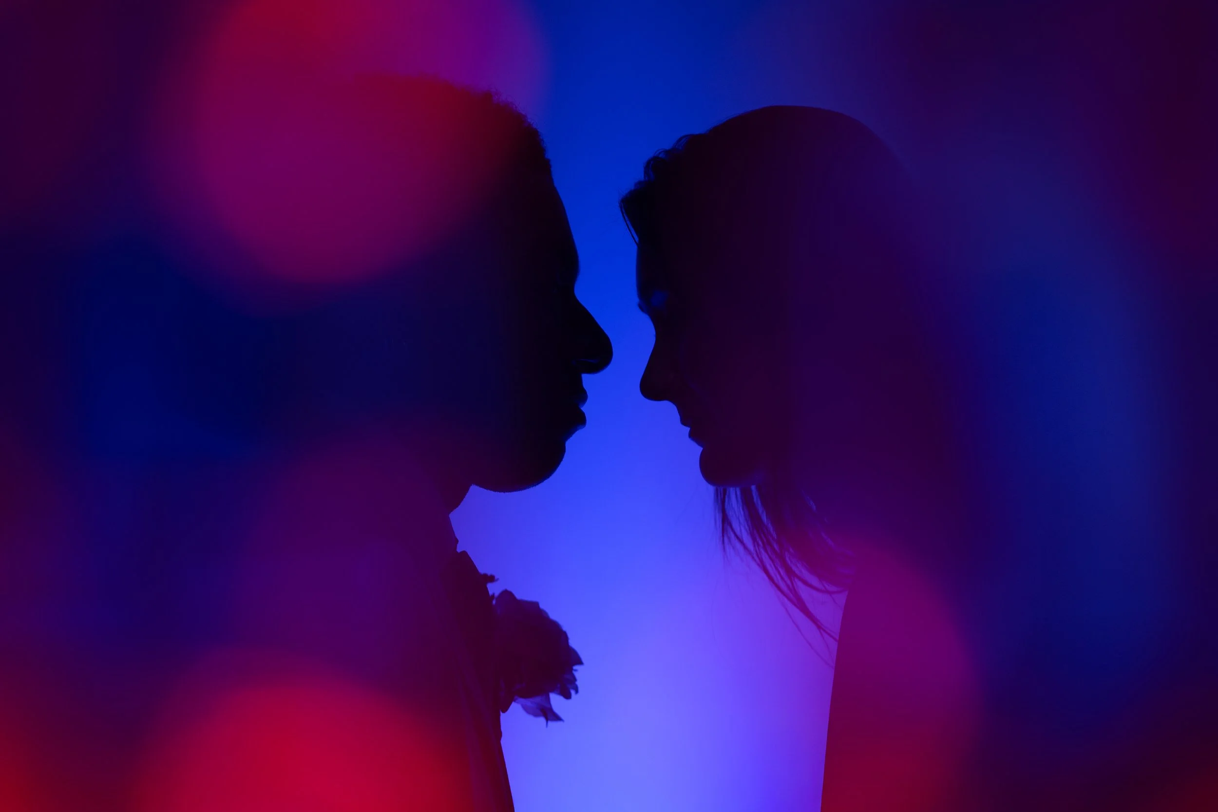 Silhouettes of two people facing each other in a colorful, abstract background with shades of purple, blue, and red.