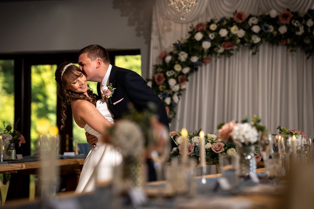 A bride and groom sharing a kiss during their wedding reception in a decorated indoor venue.
