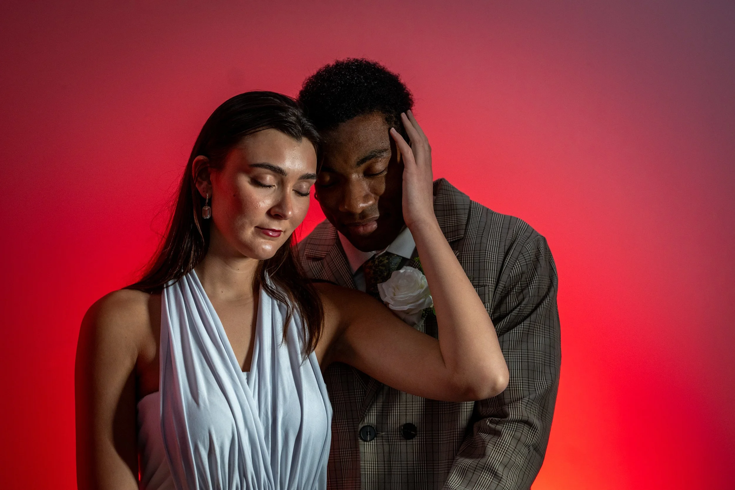 A man and woman with their eyes closed, showing an emotional moment, against a red background.