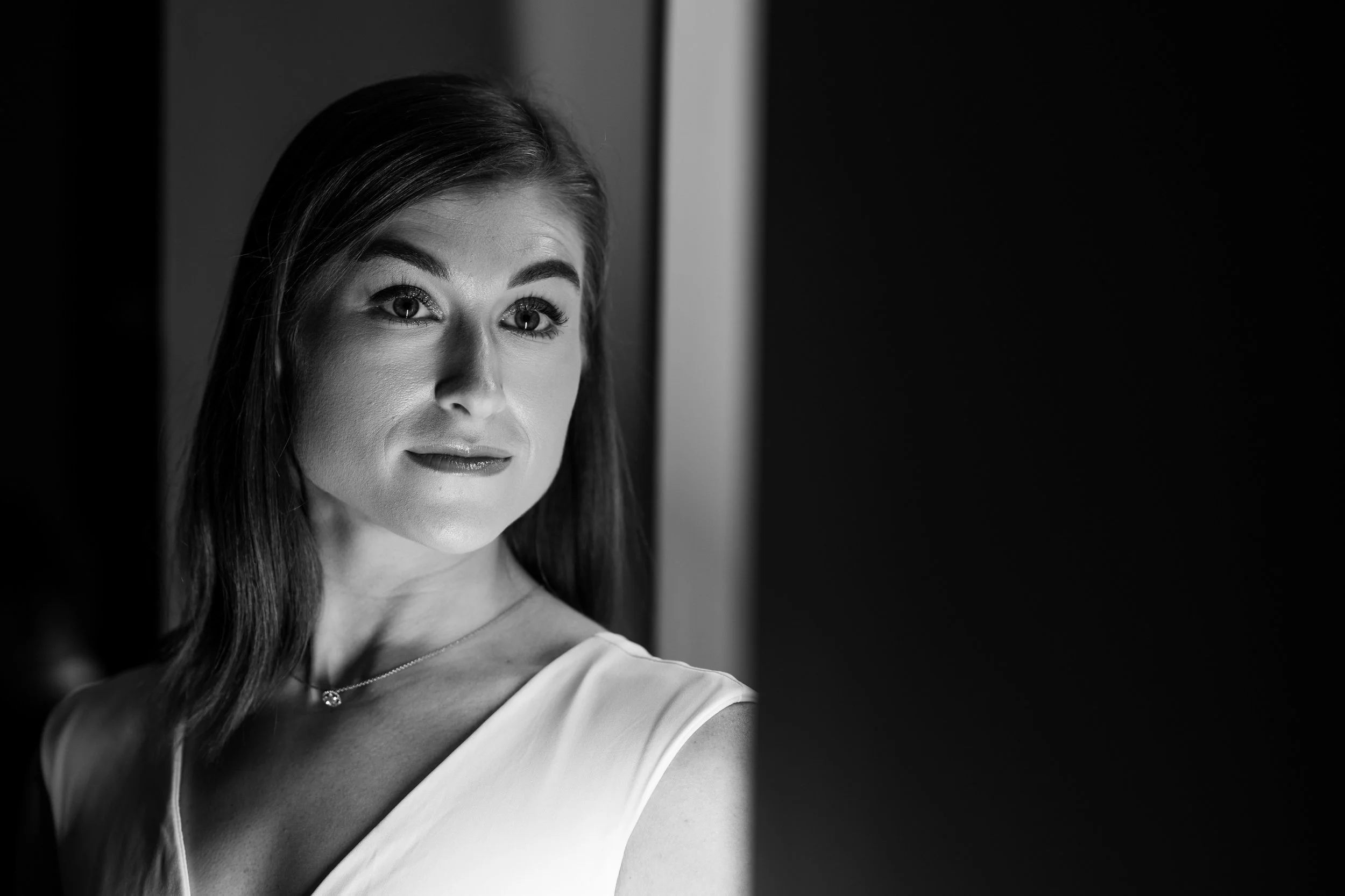 Black and white portrait of a woman with long dark hair, wearing a sleeveless top and a necklace, looking to her left.