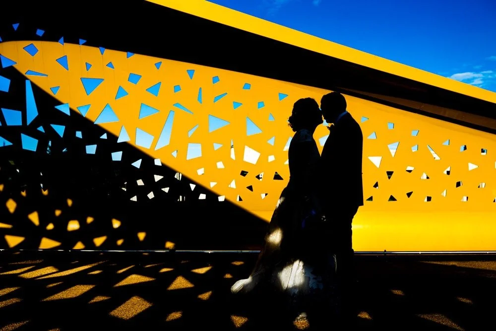 Silhouette of a couple facing each other at sunset against a modern, patterned architectural background.